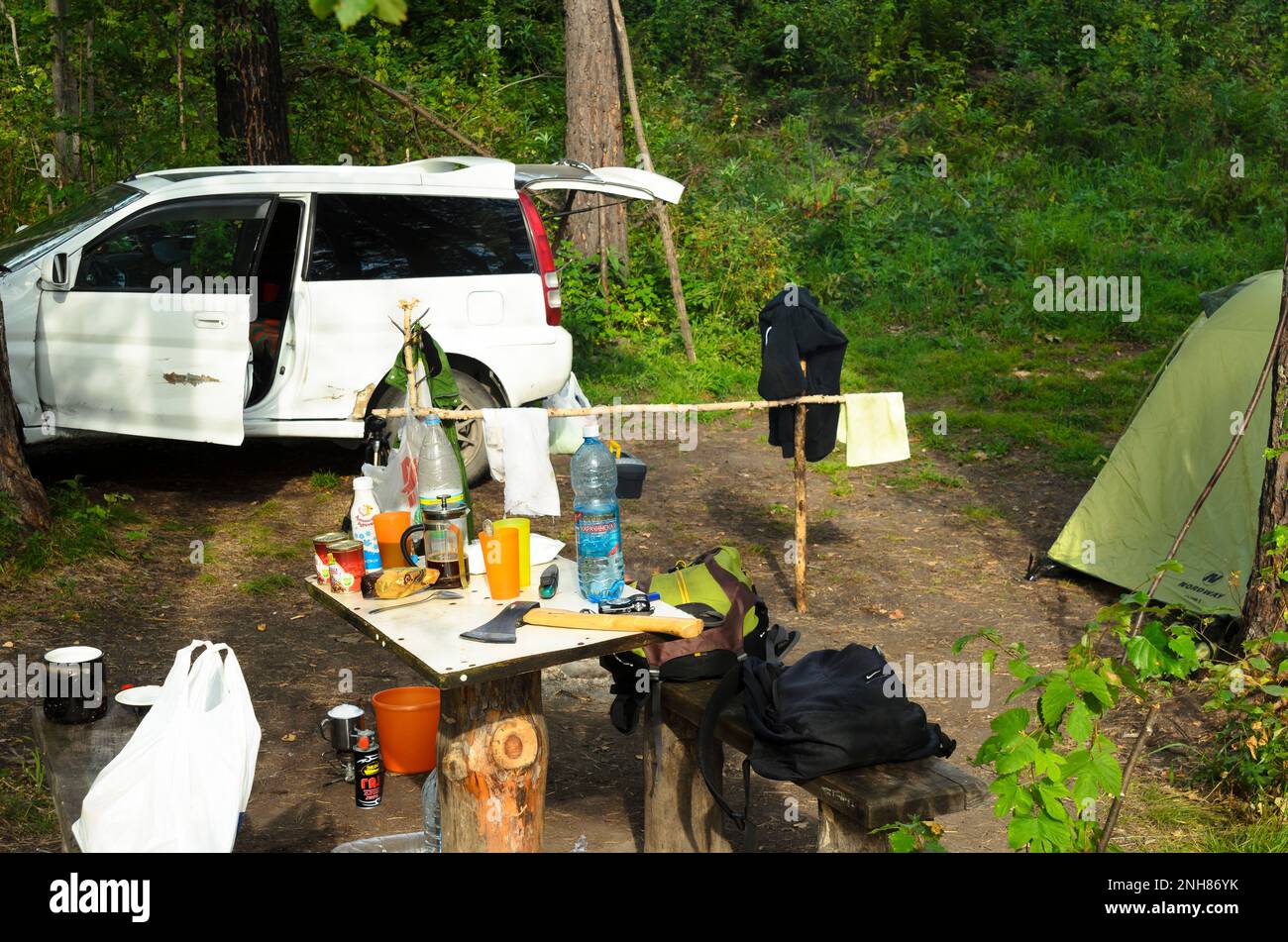 Die Marke „Honda HR-V“ steht am Campingtag in den Wäldern in der Nähe des Zelts „Nordway“ und eines Holztisches mit Essen, Wasser, Axt und Rucksäcken in Altai Stockfoto