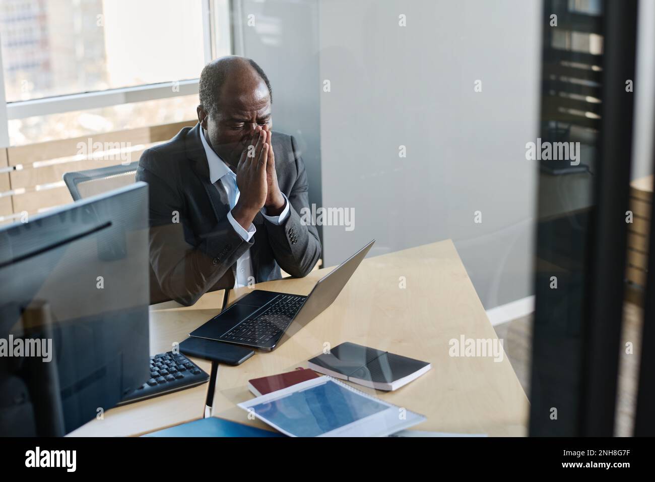 Gestresster, reifer Geschäftsmann, der seine Hände von Angesicht zu Angesicht auf den Laptop-Bildschirm blickte, während er am Arbeitsplatz in seinem Büro saß Stockfoto