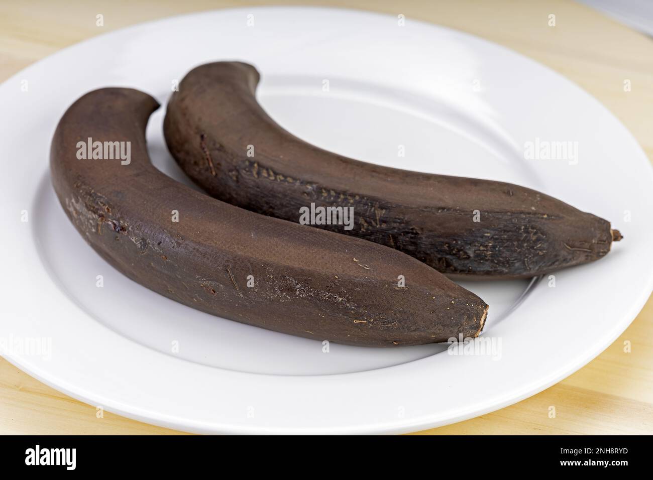 Gekühlte Bananen, die zu lange bei Raumtemperatur gelagert wurden, schwarze Schale auf einem weißen Teller. Stockfoto