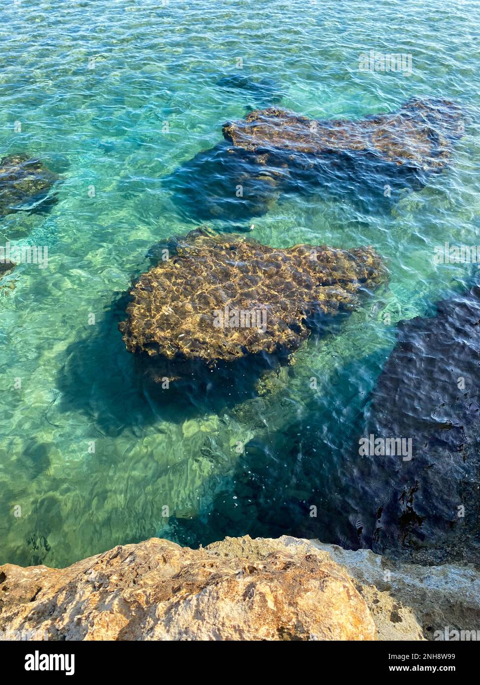 Blick von oben auf ruhiges türkisfarbenes Meerwasser und Unterwasserfelsen. Wellen auf Felsen mitten im Meer. Stockfoto