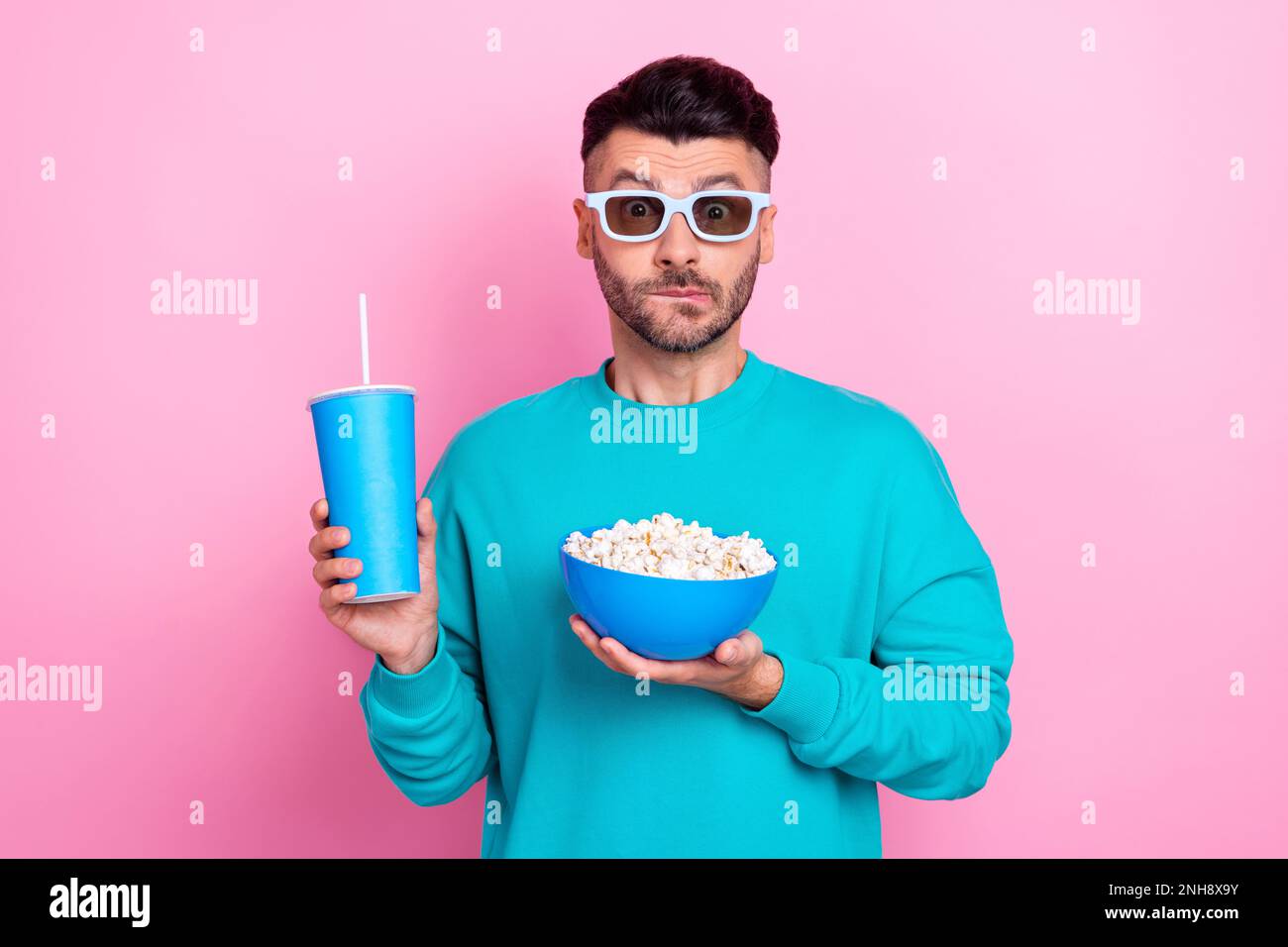 Foto eines jungen nervösen Kerls, der einen Plastikbecher mit Limonade hält, Snacks isst, Popcorn schaut euch 3D Film Panik Moment isoliert auf pinkfarbenem Hintergrund an Stockfoto