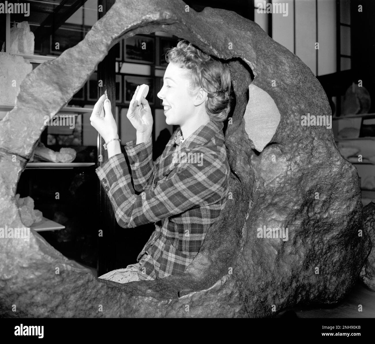Frau, die mit dem Irwin-Ainsa (Tucson-Ring)-Meteoriten im Smithsonian Museum of Natural History, Washington, D.C. posierte Dieser Tucson-Meteorit ist ein Brezinaite-Meteoritenfragment. Es wurde in den 1700er Jahren von Jesuiten-Missionaren am Fuße der Sierra de la Madera beansprucht und schließlich nach Tucson, Arizona, transportiert, wo es als eine Art öffentlicher Amboss verwendet wurde. Brezinaite ist ein seltenes Mineral, das aus Chrom und Schwefel besteht und in Meteoriten vorkommt. Harris & Ewing, Fotograf, c. 1938-39. Stockfoto