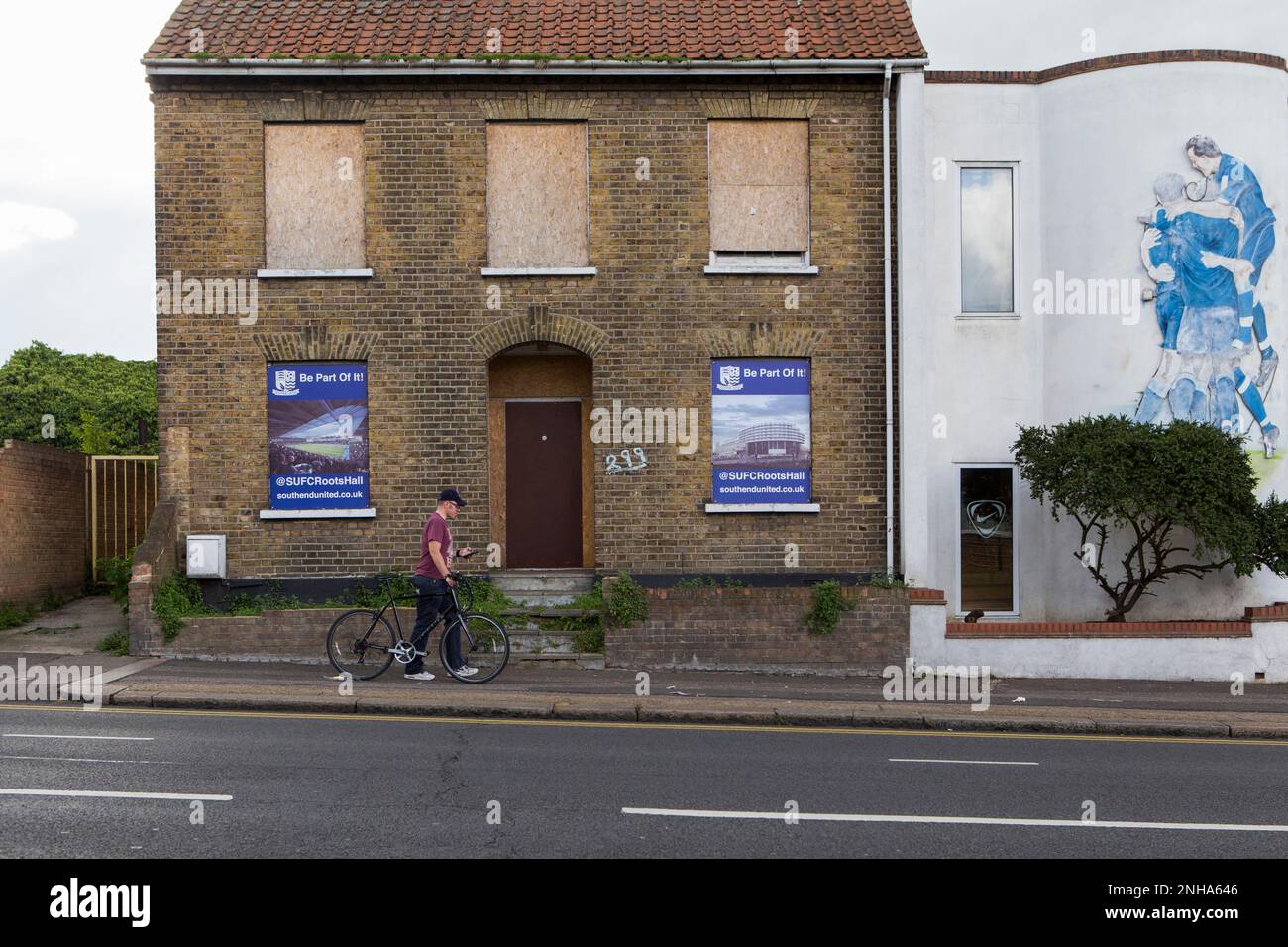 Ein Mann, der an einem heruntergekommenen Gebäude vorbeigeht, mit Plakaten, auf denen das neue Stadion des Vorsitzenden Ron Martin für den Southend United Football Club vorgestellt wird. Victoria Ave. Stockfoto