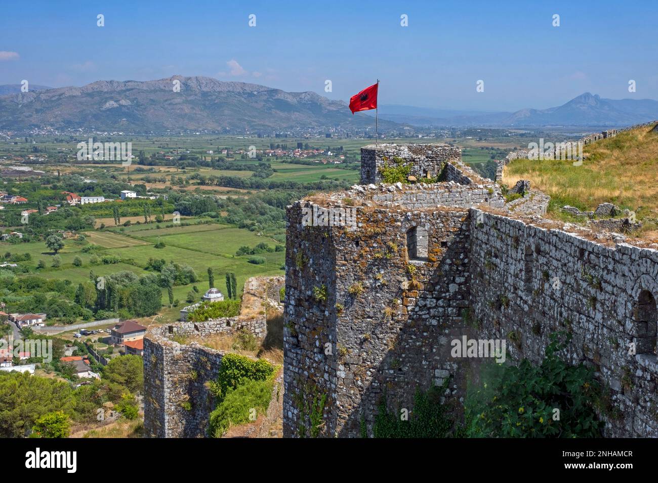 Albanische Flagge auf den Burgmauern von Schloss Rozafa/Kalaja e Rozafës und Blick auf die albanischen Alpen in der Nähe von Shkodër/Shkodra im Nordwesten Albaniens Stockfoto
