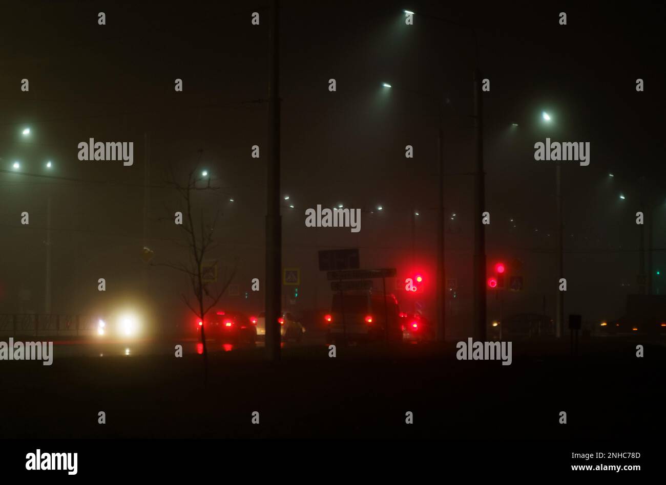 Leuchtende Ampeln und Autoscheinwerfer am Abend in einer nebligen Stadt. Stadtverkehr. Bild ist nicht scharf Stockfoto