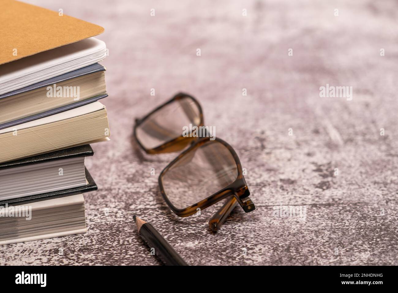 Ein Stapel alter Bücher mit Brille und einem schwarzen Bleistift mit unscharfem Hintergrund Stockfoto