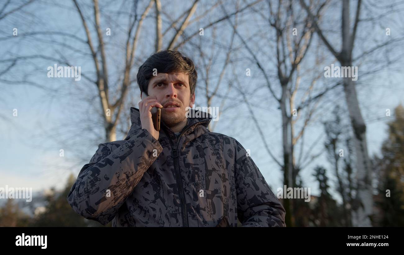 Junger Mann in einer stylischen schwarzen Sportjacke, der im Freien einen ernsthaften Telefonanruf führte, demonstrierte Engagement und Zuverlässigkeit bei der Geschäftskommunikation Stockfoto