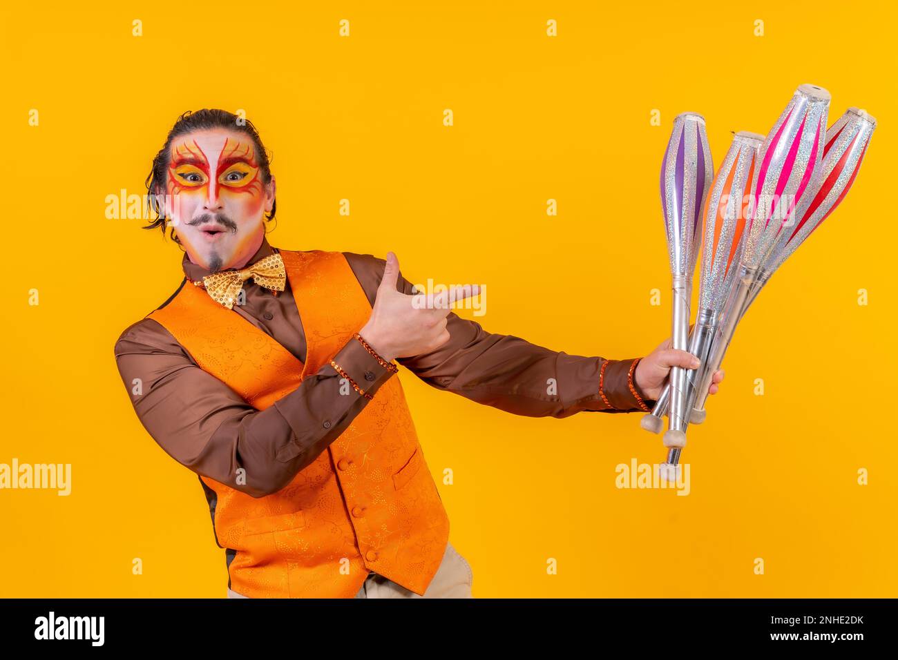 Porträt eines glücklichen Jongleurs in Make-up-Weste, der mit Maces auf gelbem Hintergrund jongliert Stockfoto