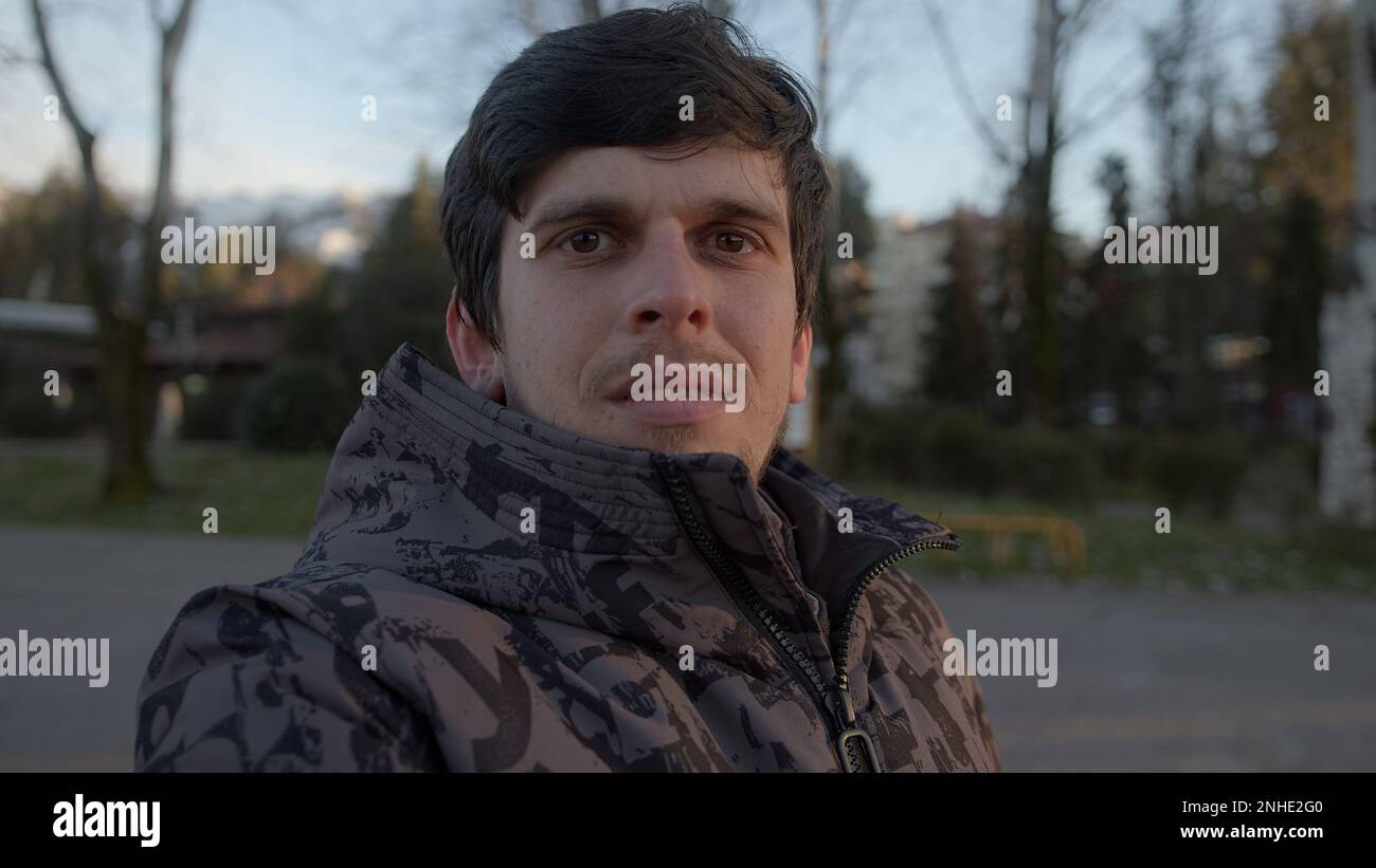Porträt eines gutaussehenden jungen Mannes in einem stylischen Mantel, der in der Kamera im Freien lächelt Stockfoto