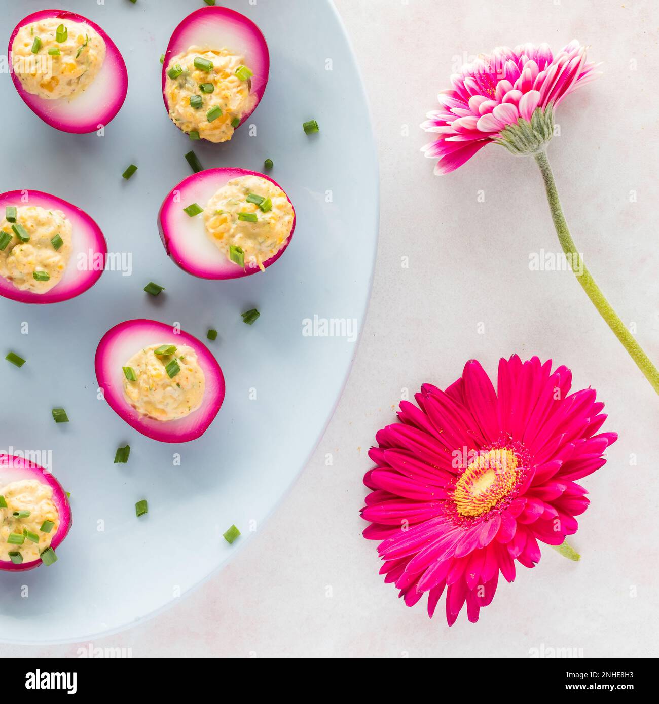 Eine Platte mit leuchtend pinkfarbenen teuflischen Eiern und zwei leuchtend pinkfarbenen Blumen. Stockfoto