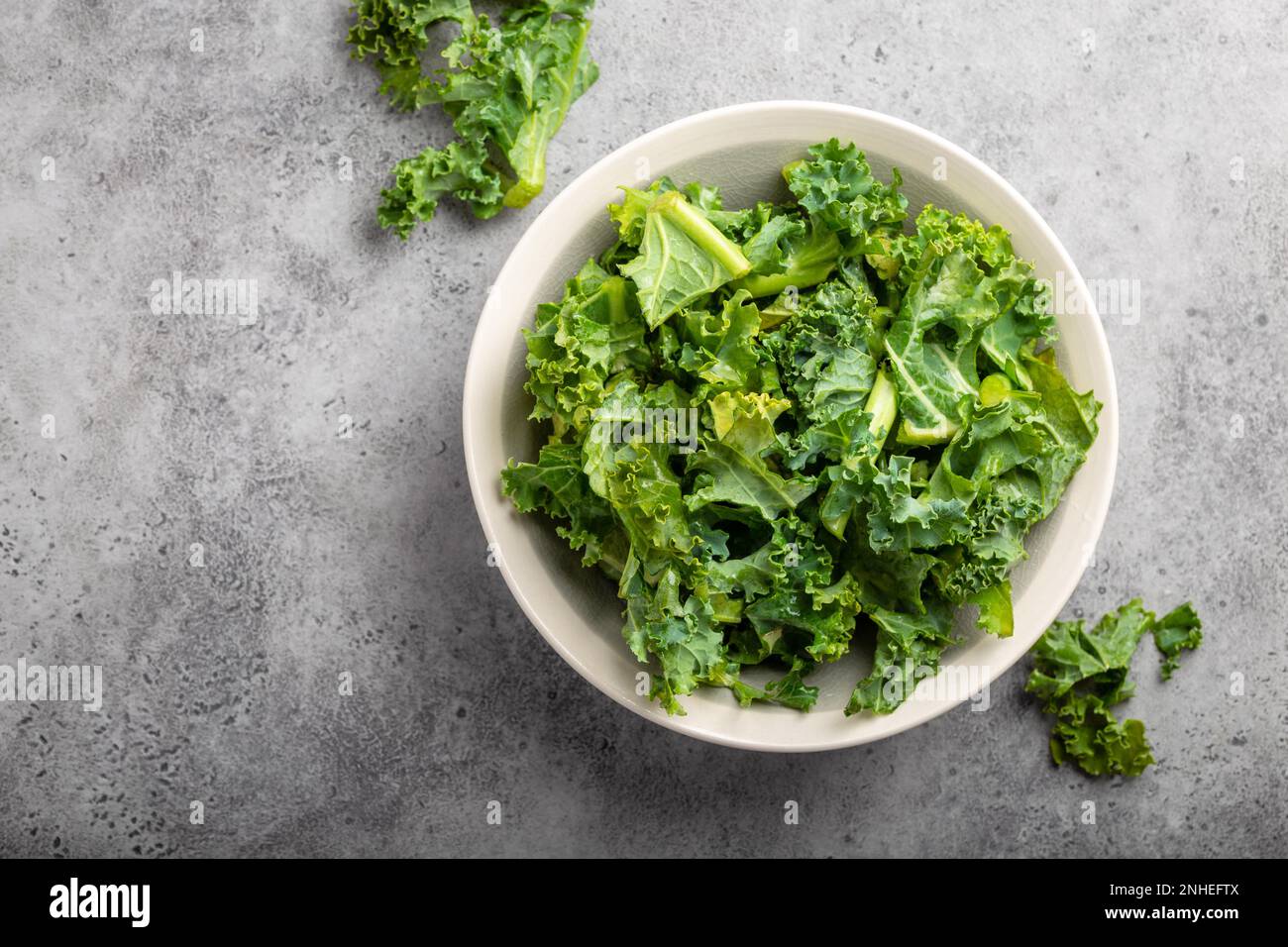 Schüssel mit frischem Grünkohl auf grauem rustikalem Steinhintergrund, Draufsicht, Nahaufnahme. Zutat für die Herstellung von gesundem Salat. Sauberes Essen, Entgiftung oder Stockfoto