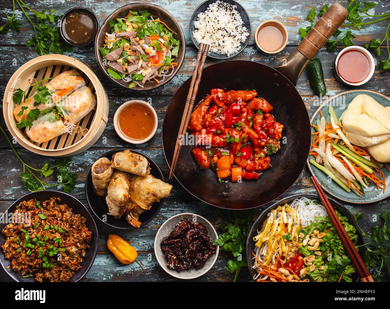 Set aus verschiedenen chinesischen Gerichten auf dem Tisch: Süßes und saures Hähnchen in der Wok-Pfanne, Dim Sum in Bambusdampfer, Frühlingsrollen, Nudeln, Salat, Reis, Gedämpft Stockfoto