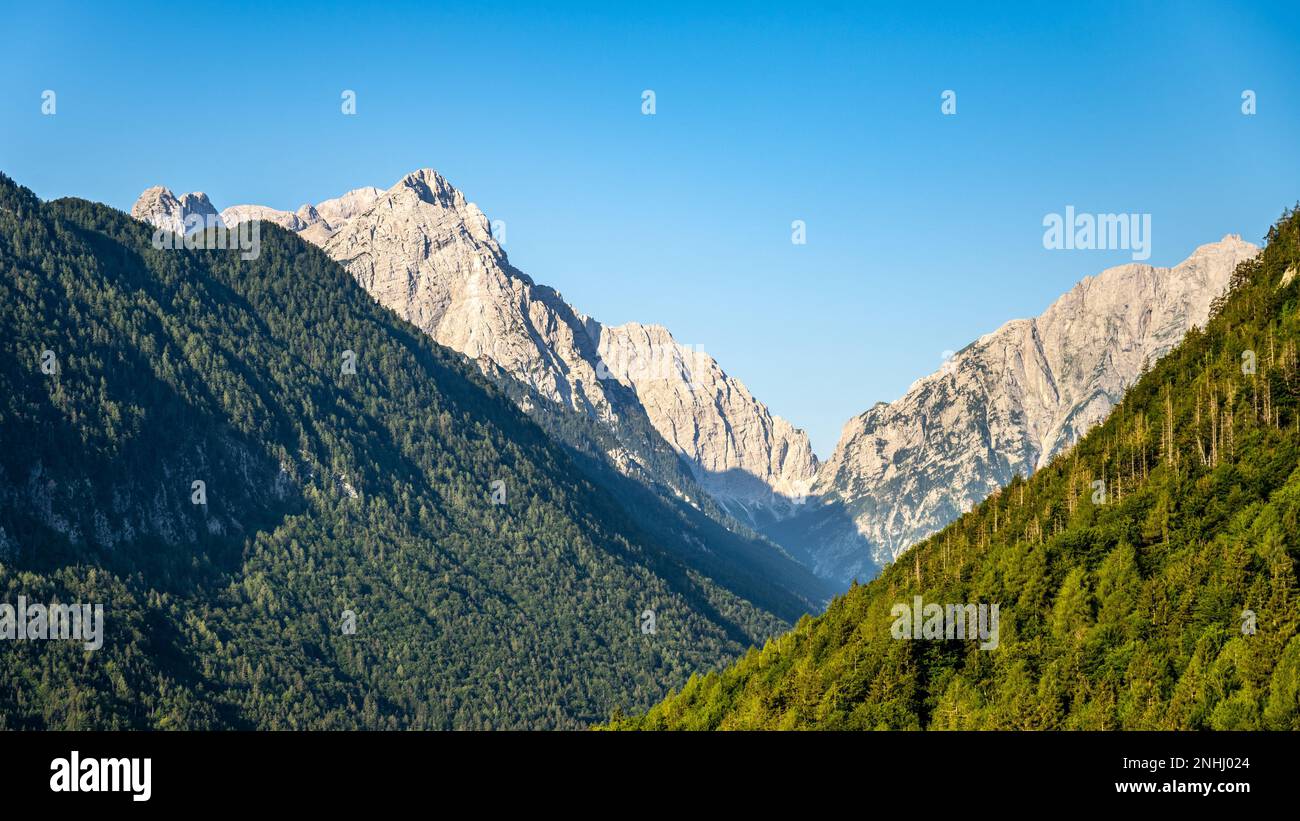 Triglav, der höchste Berg in Slowenien. Blick vom Vrata-Tal auf den felsigen Gipfel und bewaldeten Hängen der umliegenden Hügel an einem klaren Sommertag Stockfoto