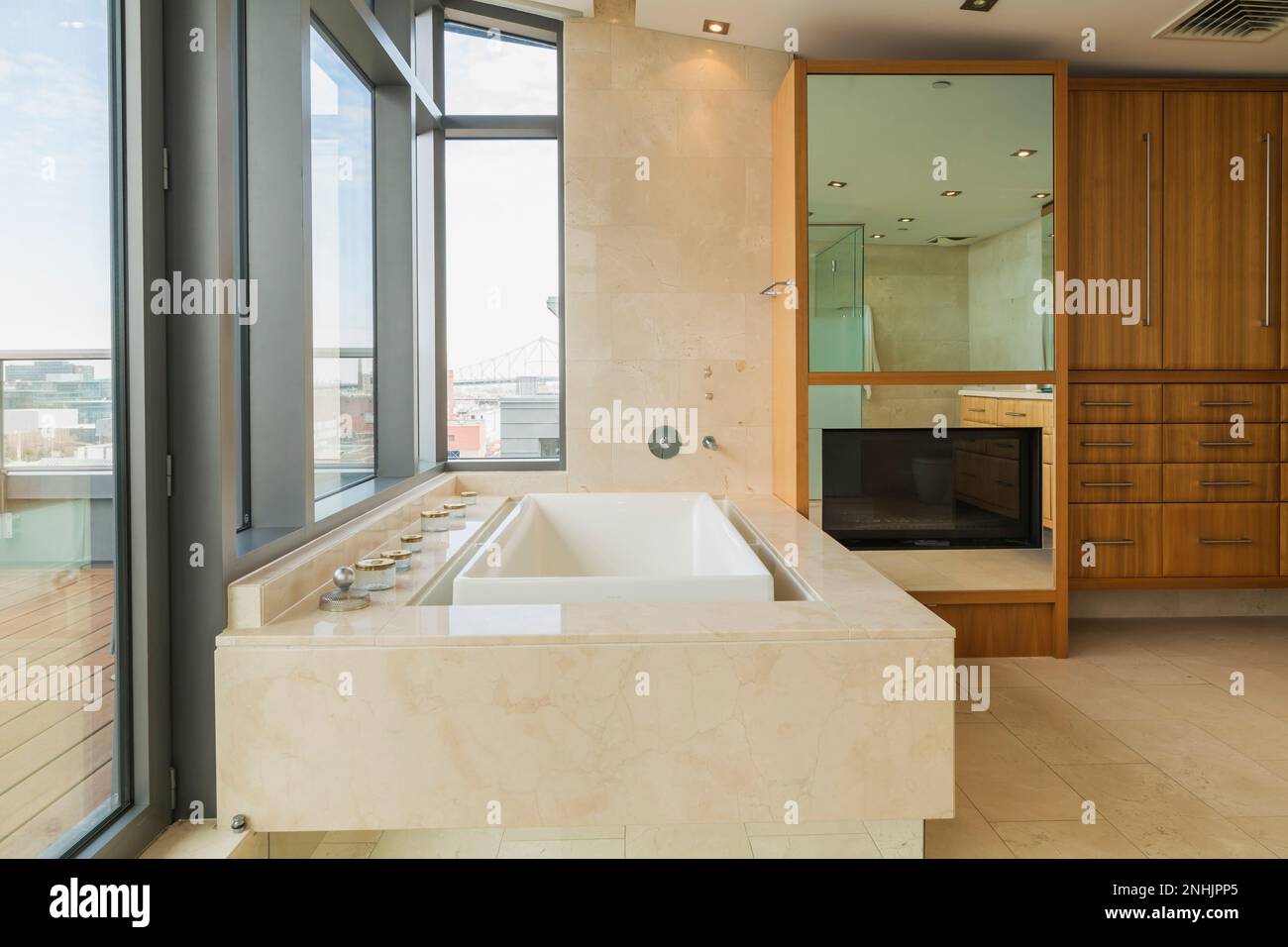 Weiße Badewanne mit Marmorhülle plus Spiegel mit eingebautem Breitbildfernseher in en Suite mit Marmorfliesenboden in moderner luxuriöser Wohnung. Stockfoto