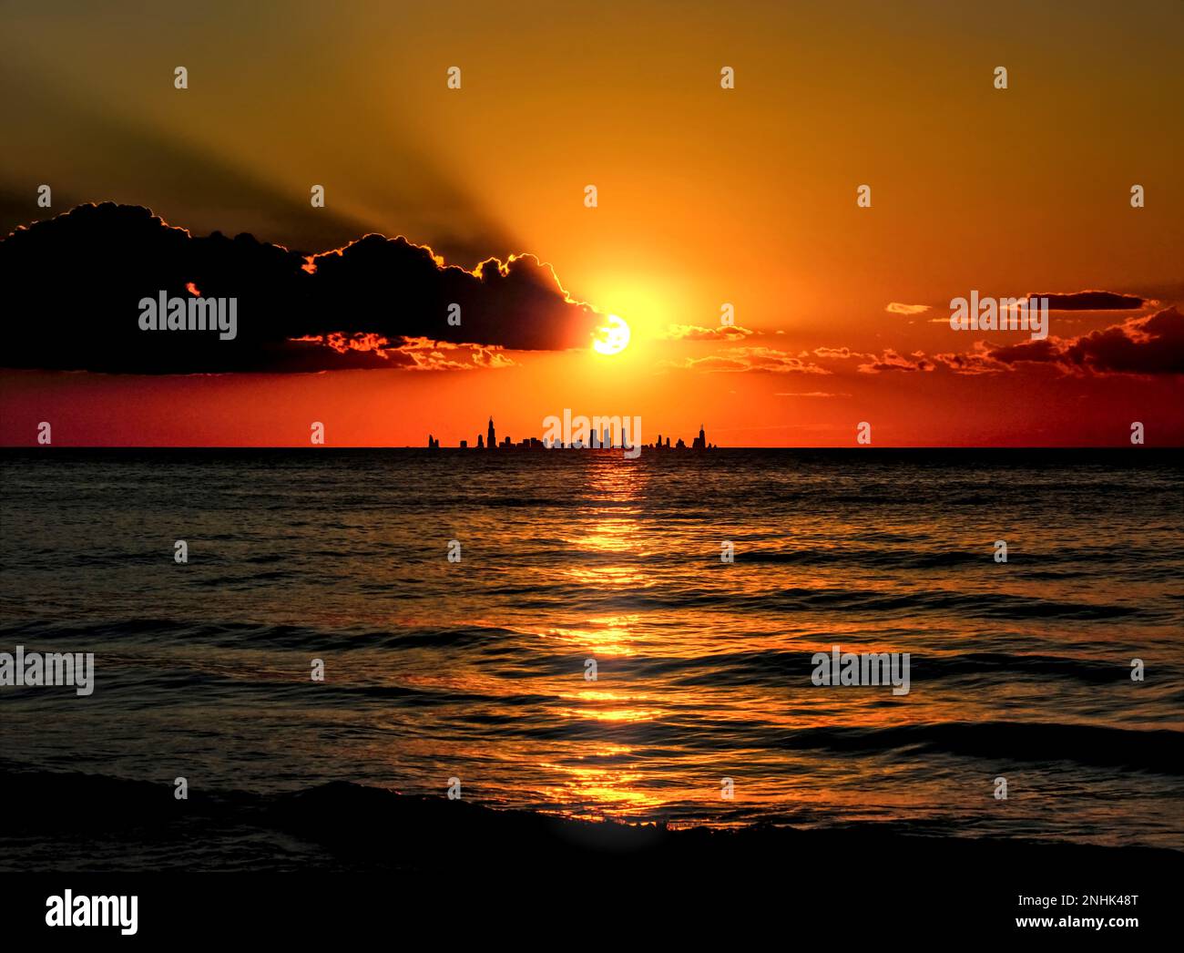 Die Skyline von Chicago bei Sonnenuntergang vom Dunes National Park über den Lake Michigan aus in Silhouette. Starke, krepuskuläre Strahlen und goldgesäumte Wolken. Stockfoto