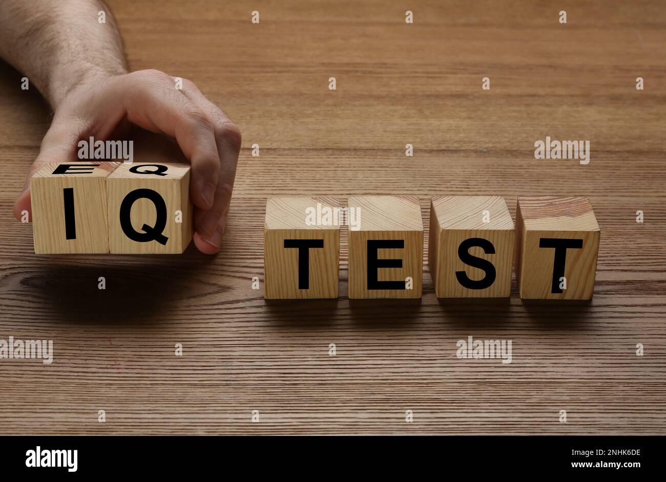 Mann nimmt Würfel mit Text IQ Test auf Holz Hintergrund, Nahaufnahme Stockfoto