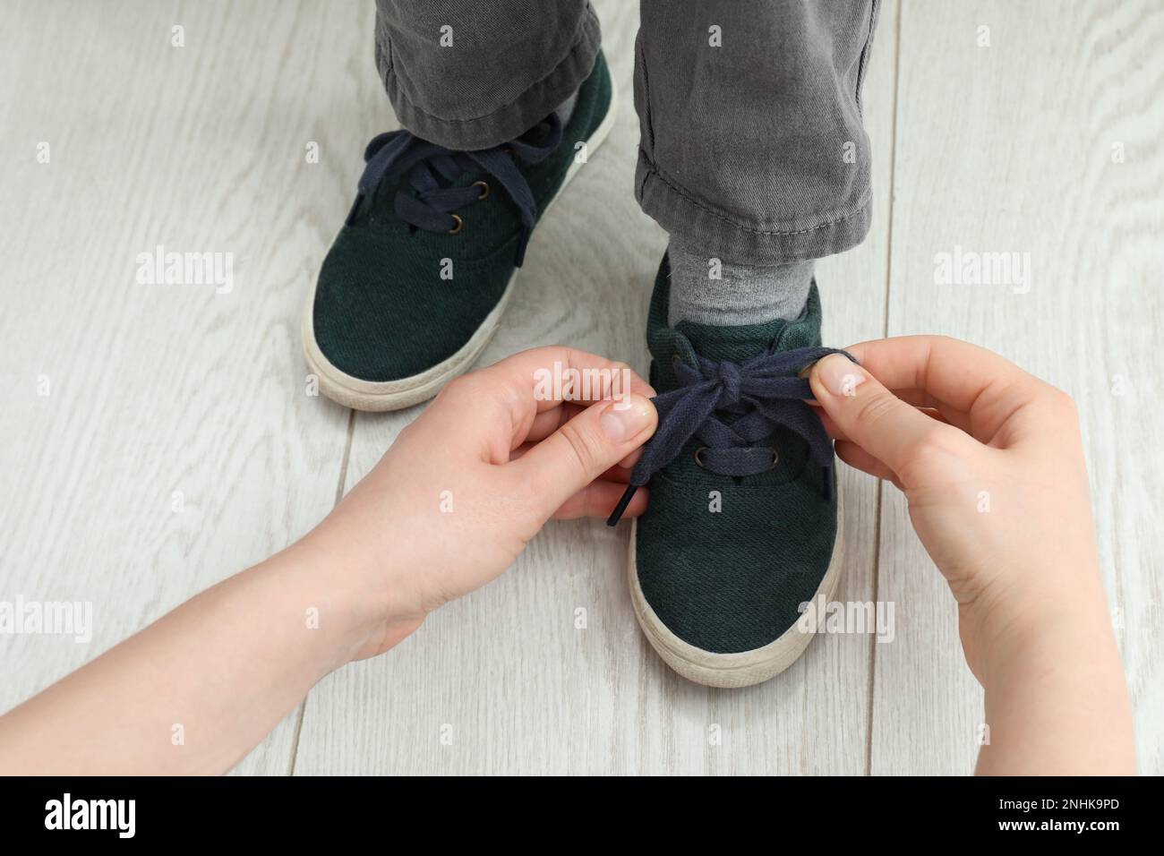 Mutter hilft dem Sohn, zu Hause Schnürsenkel zu binden, Nahaufnahme Stockfoto