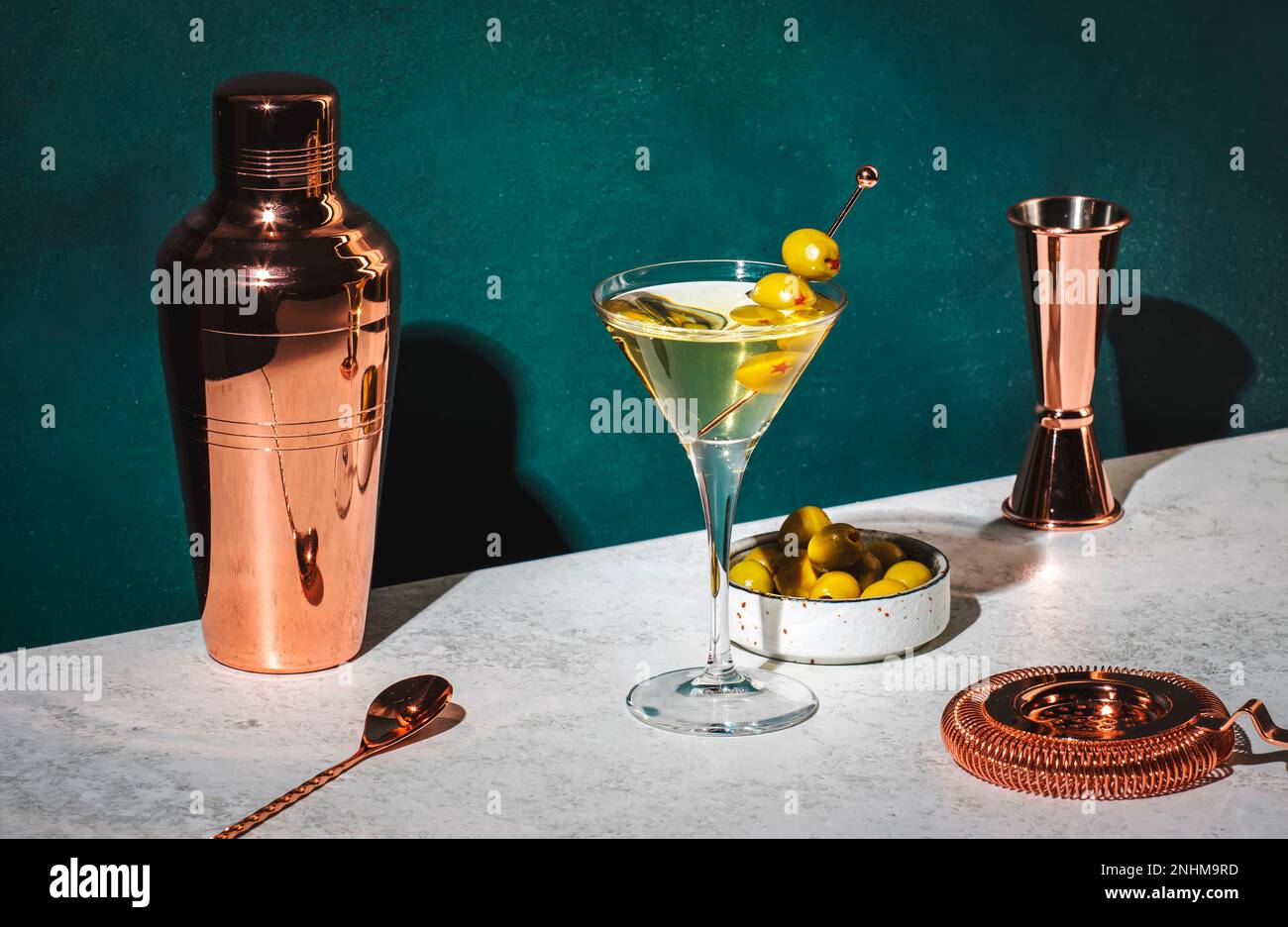 Wodka martini, klassisches alkoholisches Cocktailgetränk mit Wodka und Wermut, Garnierung grüner Oliven, dunkler Hintergrund, helles, hartes Licht und Schattenmuster Stockfoto