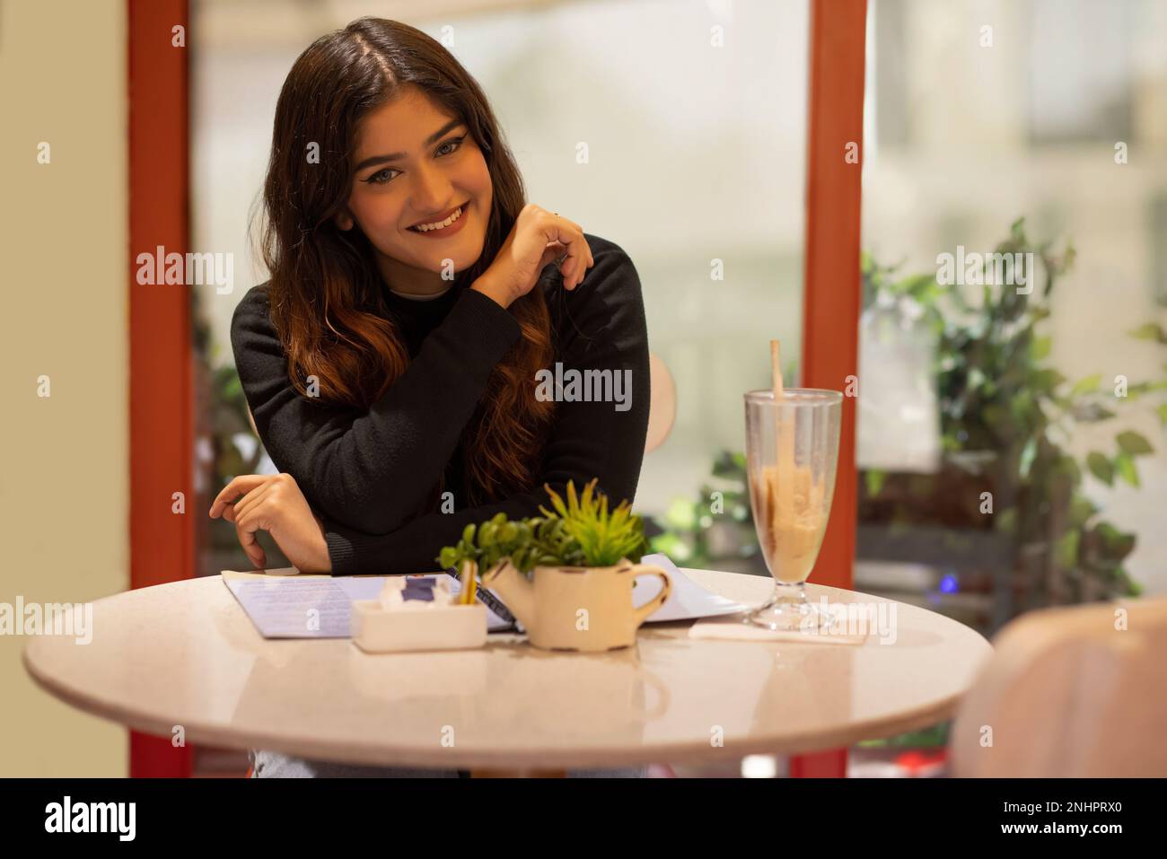 Fröhliche junge Frau, die in die Kamera schaut, während sie im Café sitzt Stockfoto
