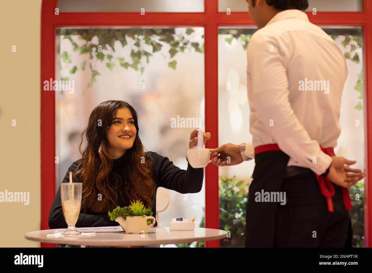 Junge Frau, die die Rechnung vom Kellner im Café annimmt Stockfoto