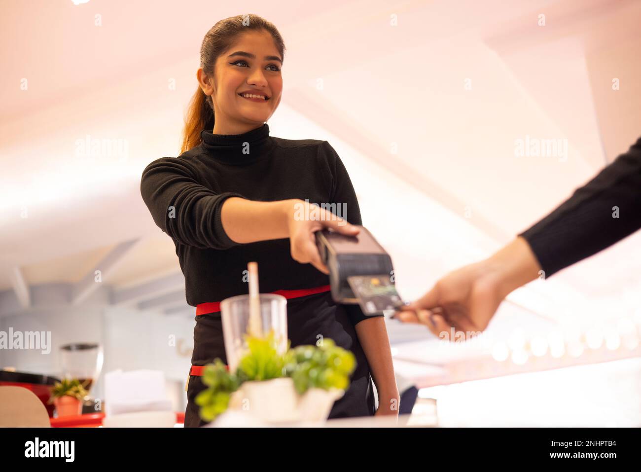 Die Kellnerin hält den Kartenleser, während der Gast die Zahlung per Kreditkarte vornimmt Stockfoto
