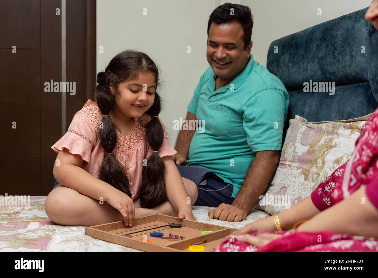 Ein kleines Mädchen, das einen schnellen Sling-Puck spielt, und ein Vater, der neben dem Bett sitzt Stockfoto