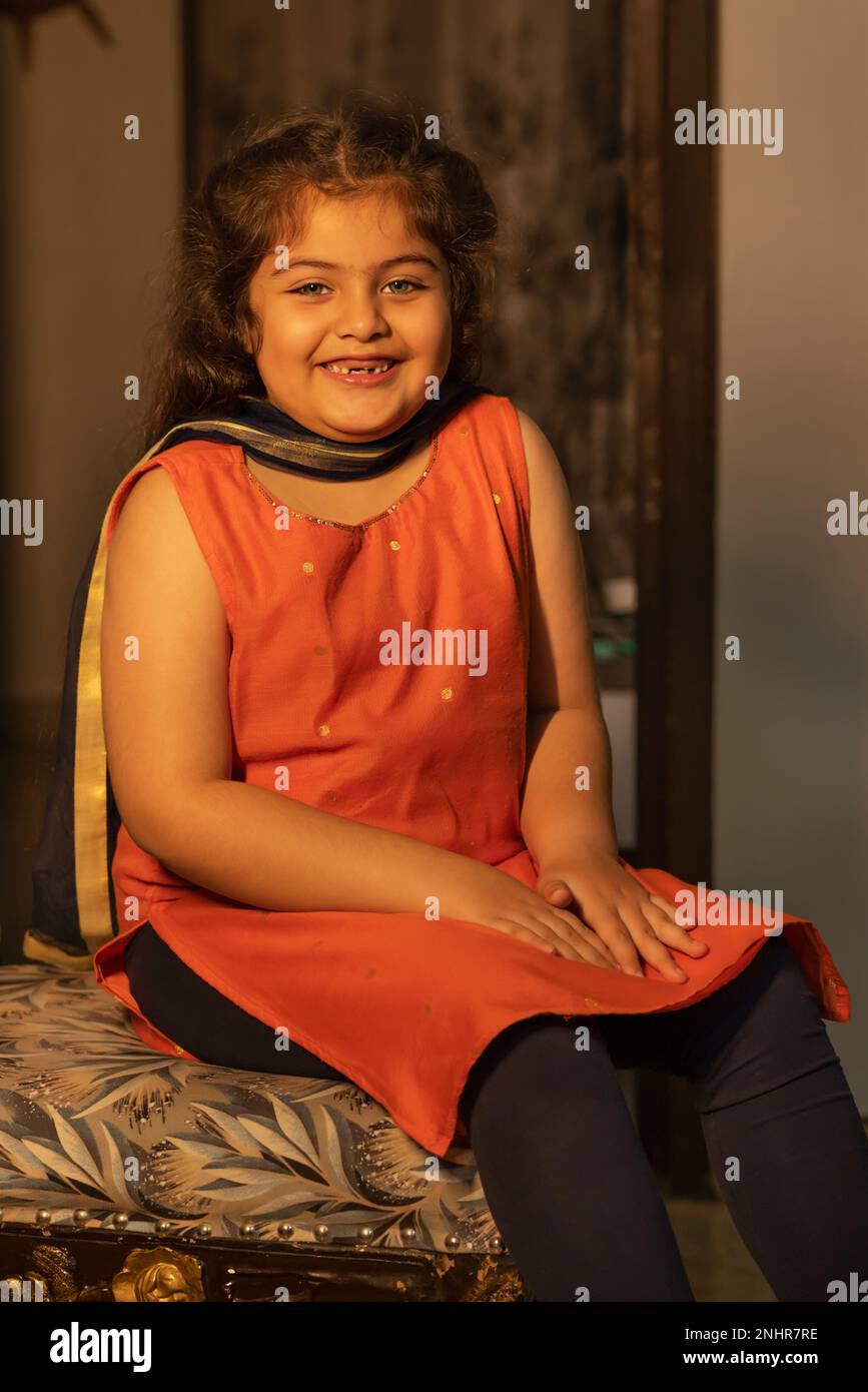 Porträt eines lächelnden kleinen Mädchens, das zu Hause auf einem Stuhl sitzt Stockfoto