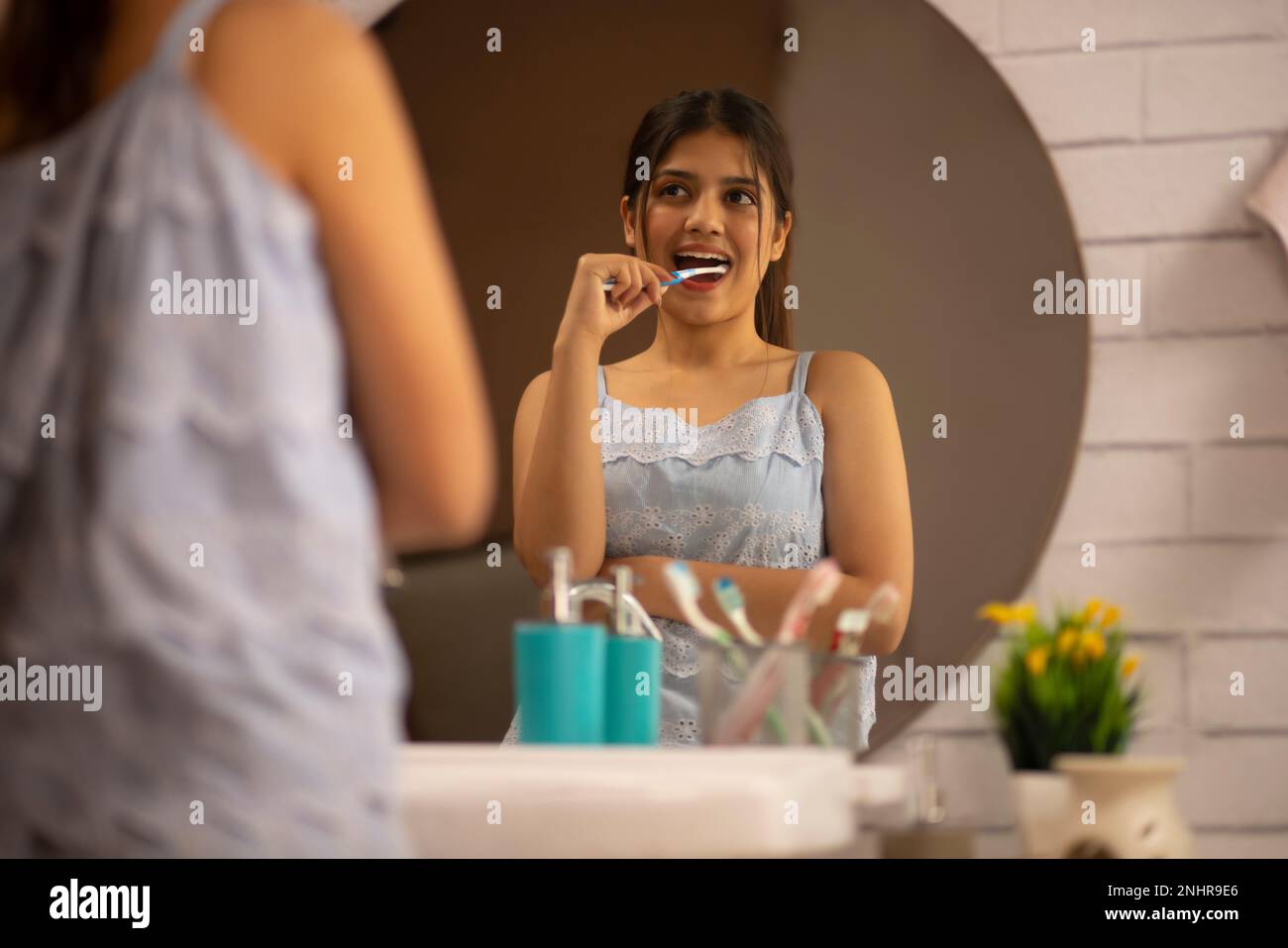 Junge Frau, die im Spiegel steht, während sie sich im Bad die Zähne putzt Stockfoto