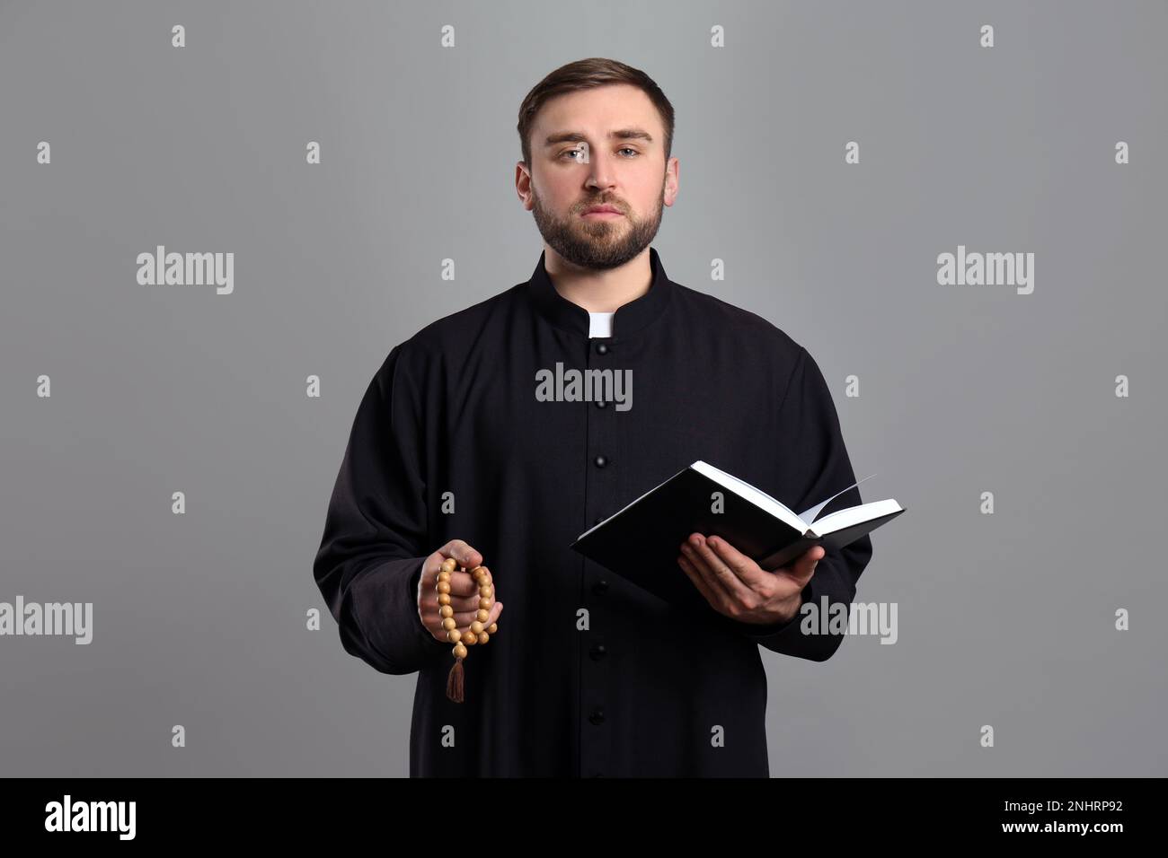 Priester mit Perlen und Bibel betet auf grauem Hintergrund Stockfoto