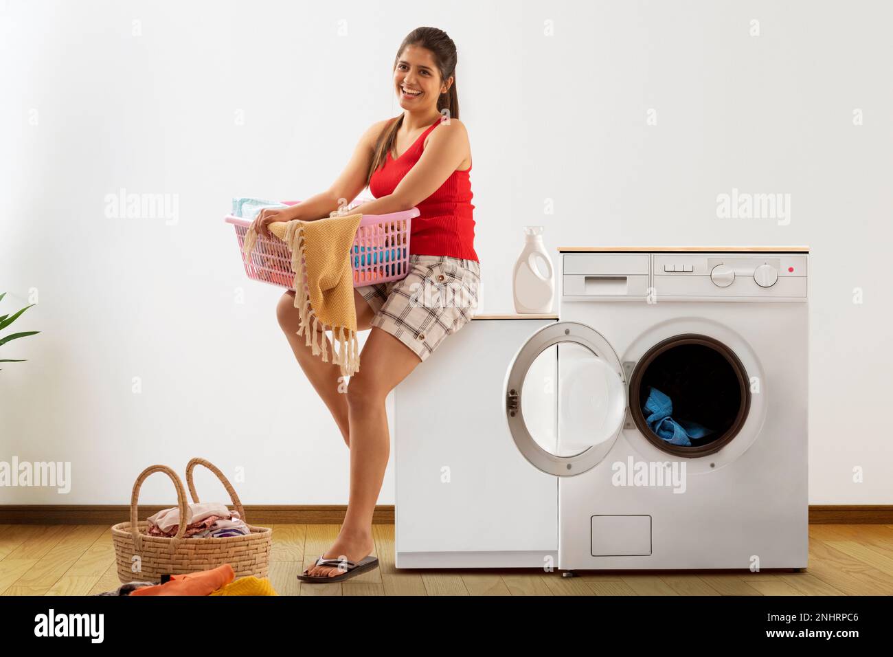 Junge Frau, die neben der Waschmaschine sitzt, mit Wäschekorb Stockfoto