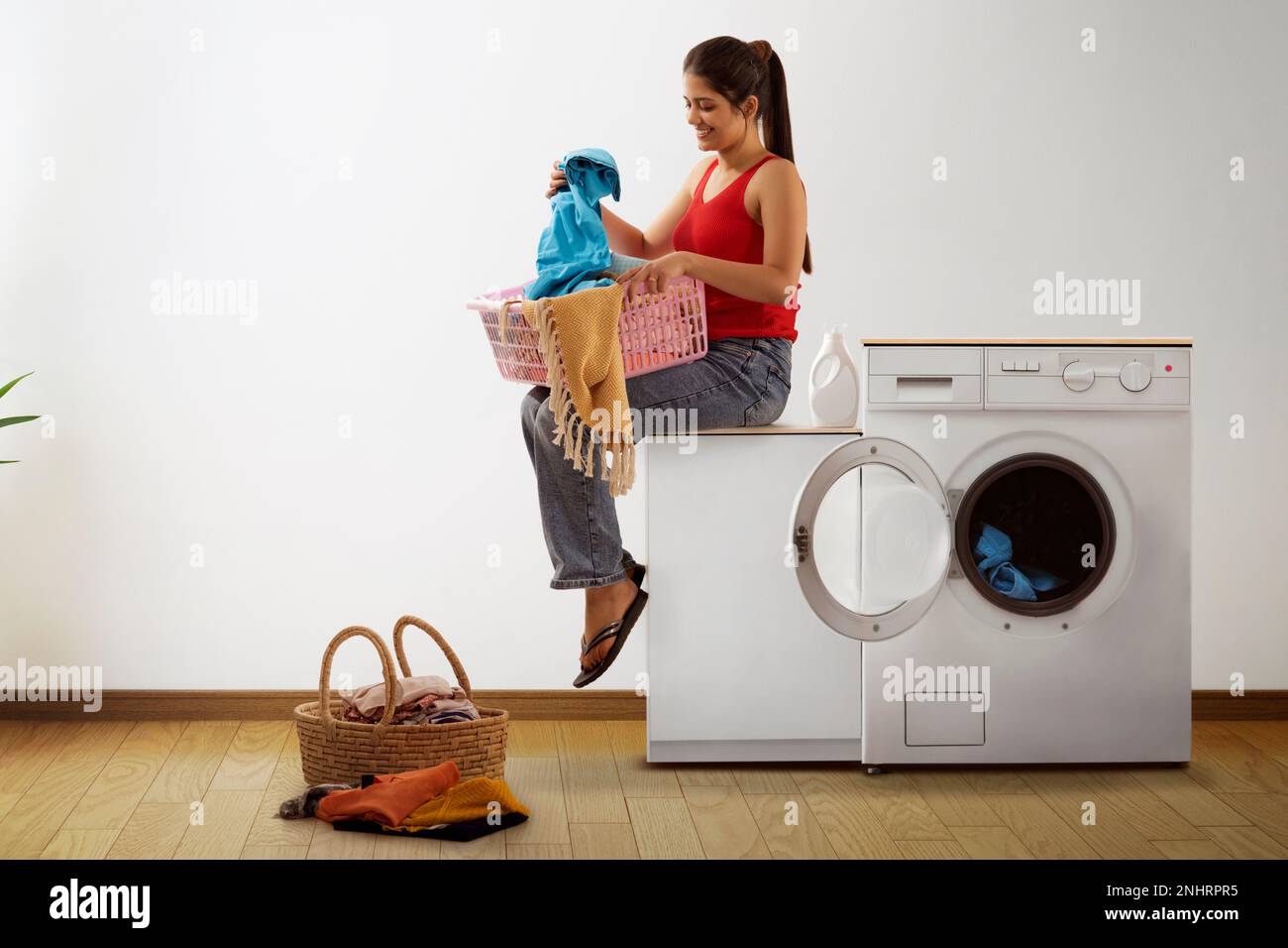 Junge Frau, die neben der Waschmaschine sitzt, mit Wäschekorb Stockfoto