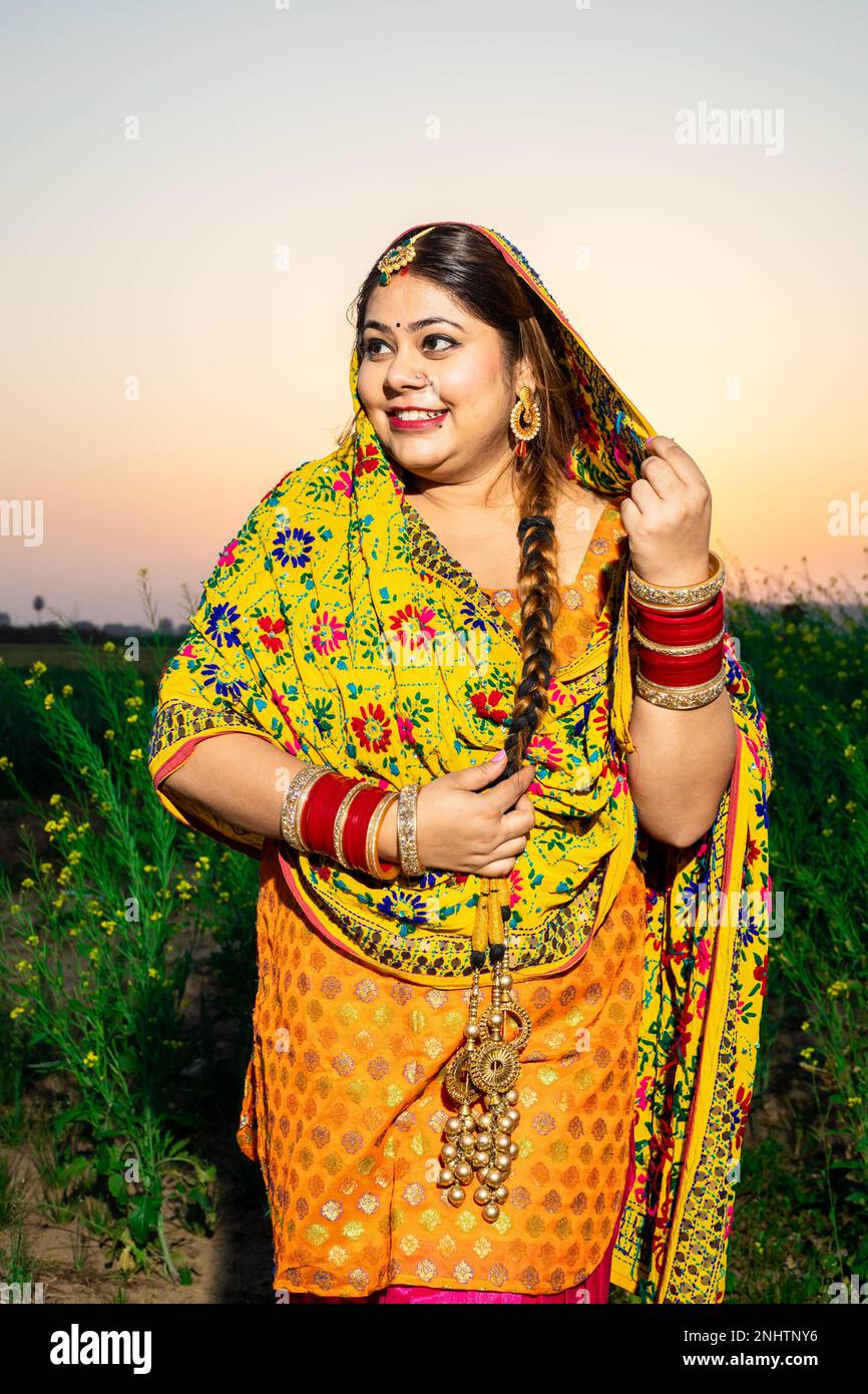 Porträt einer wunderschönen jungen indischen Frau aus punjabi, die auf dem Feld im Freien bunt und traditionell steht. Stockfoto