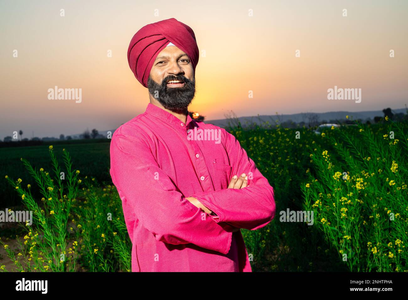 Porträt eines glücklichen jungen bauern aus punjabi sikh, der mit roten Turban und Kurta auf dem Feld vor der Kamera steht. Stockfoto