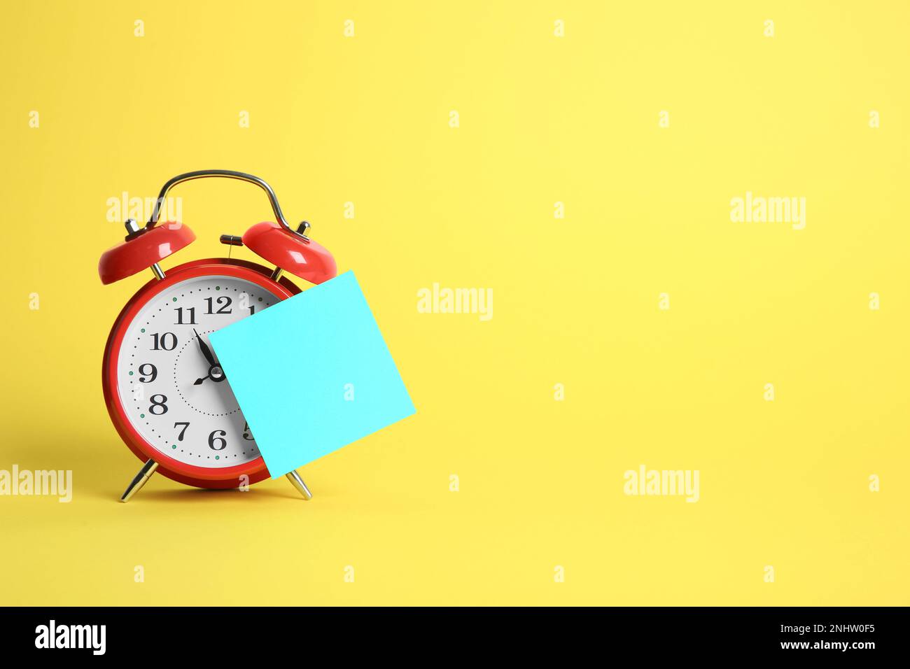 Wecker und leere Erinnerungsnotiz auf gelbem Hintergrund, Platz für Text Stockfoto
