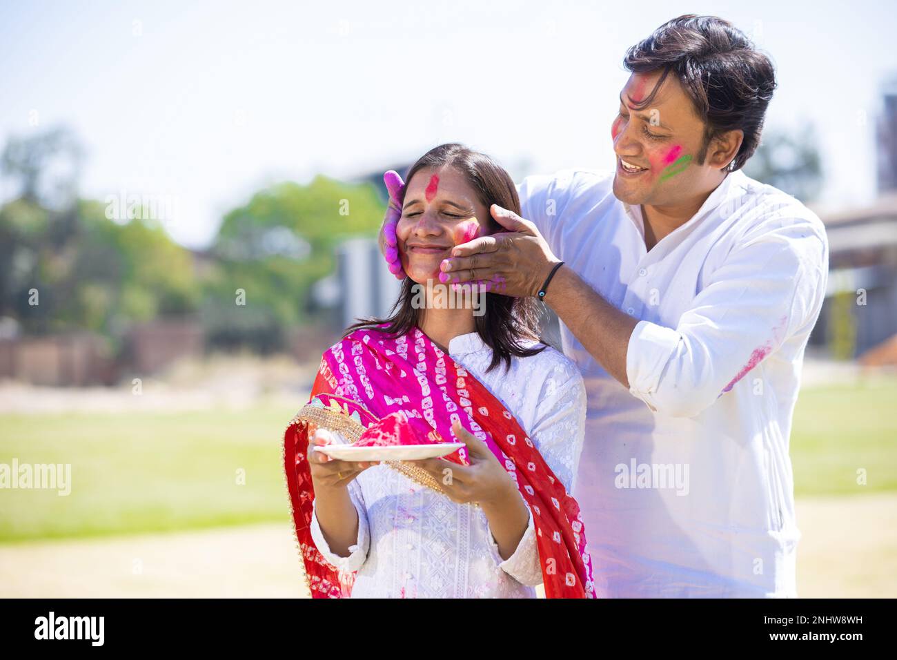 Ein glückliches, junges indianisches Paar, das weiße Kurta trägt und im Park zusammen holi feiert. Stockfoto