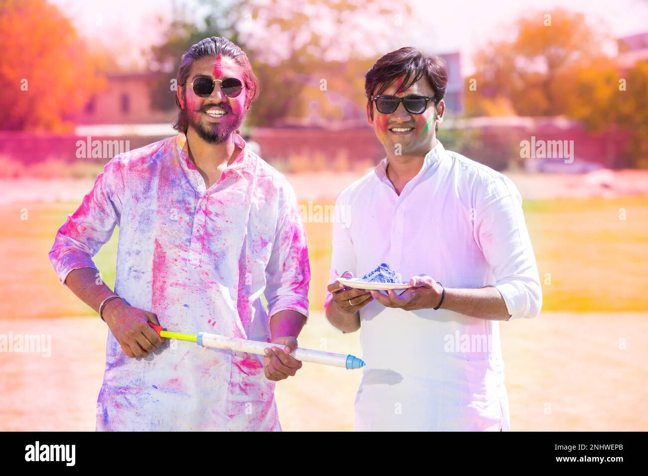 Portrait von glücklichen jungen indischen Männern, die einen weißen Kurta-Halteteller voller Pulverfarbe tragen und Pichkari, die das holi-Festival im Park Outdoor feiern, Face Stockfoto