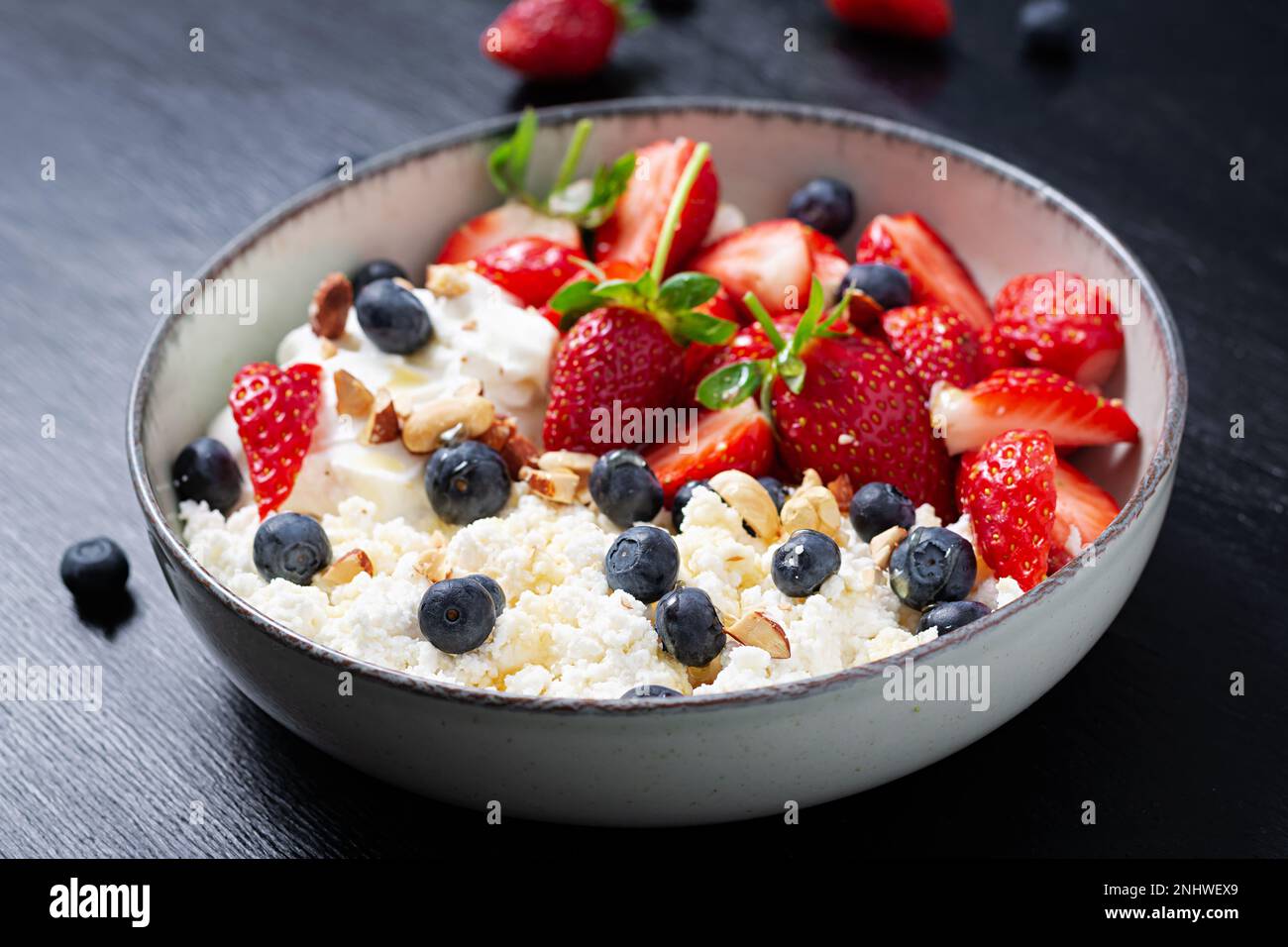 Hüttenkäse, Quark mit frischen Erdbeeren, Heidelbeeren, Nüssen und Joghurt in einer Schüssel. Gesundes Milchprodukt reich an Kalzium und Protein. Stockfoto