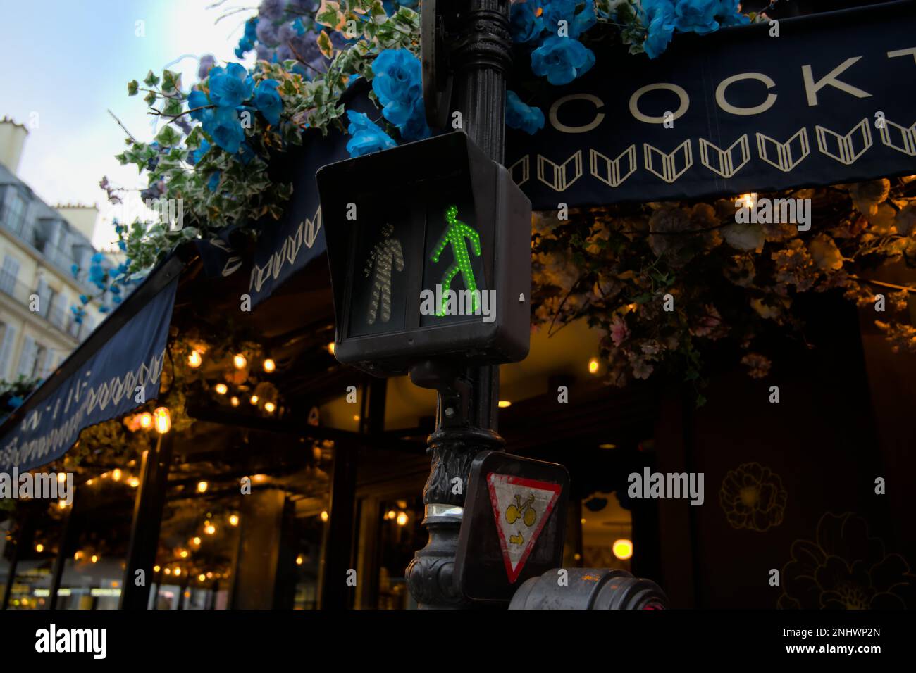 Grüne Fußgängerampel mit blauen Blumen umgeben sie in den Straßen von Paris Stockfoto