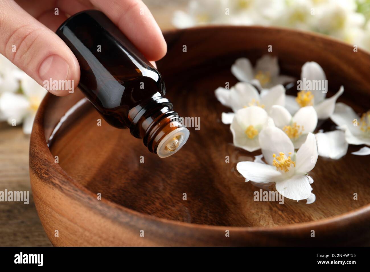 Eine Frau tropft ätherisches Jasminöl in eine Holzschüssel auf dem Tisch, Nahaufnahme Stockfoto