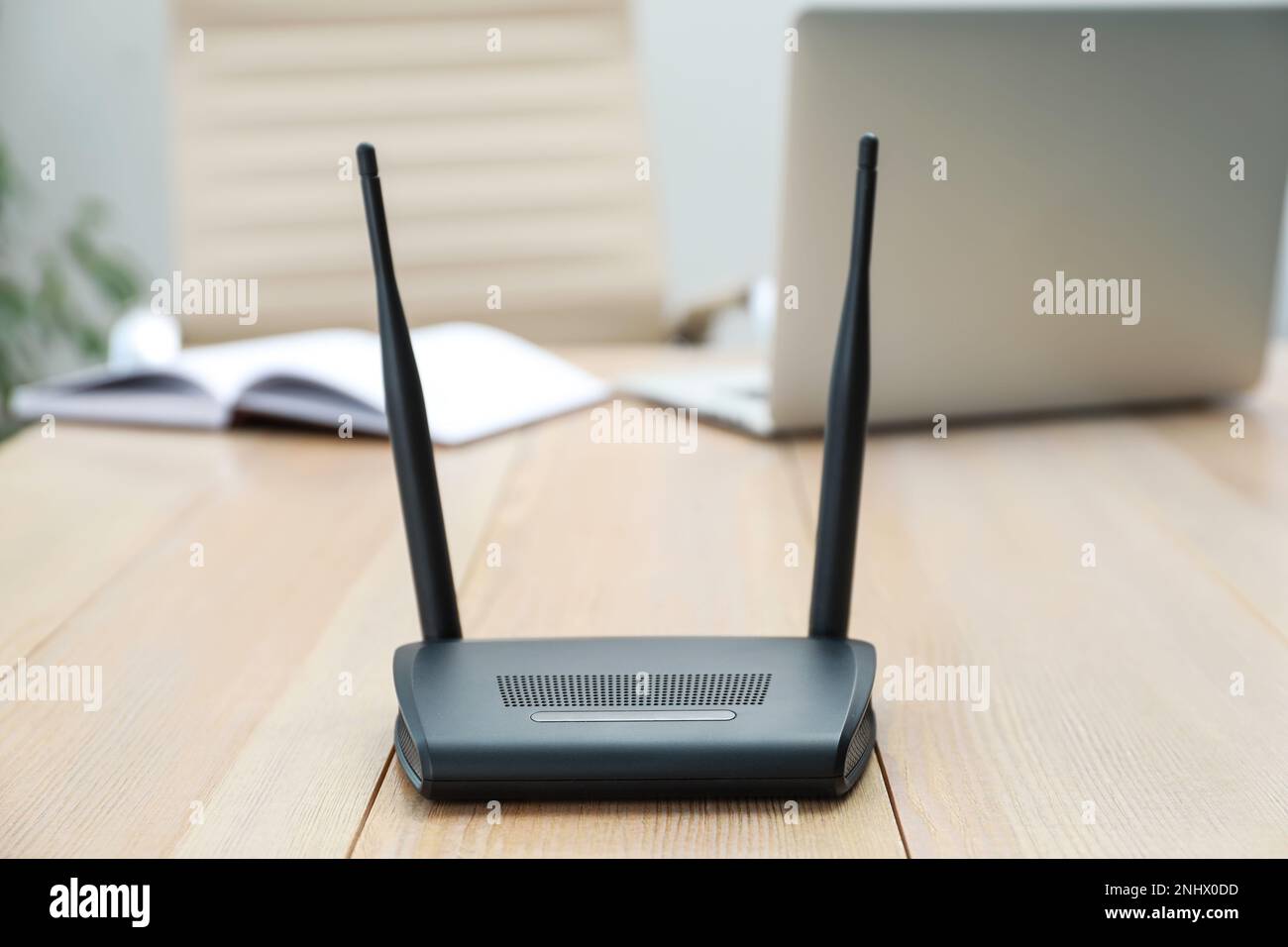 Moderner WLAN-Router auf Holztisch mit Laptop im Innenbereich Stockfoto