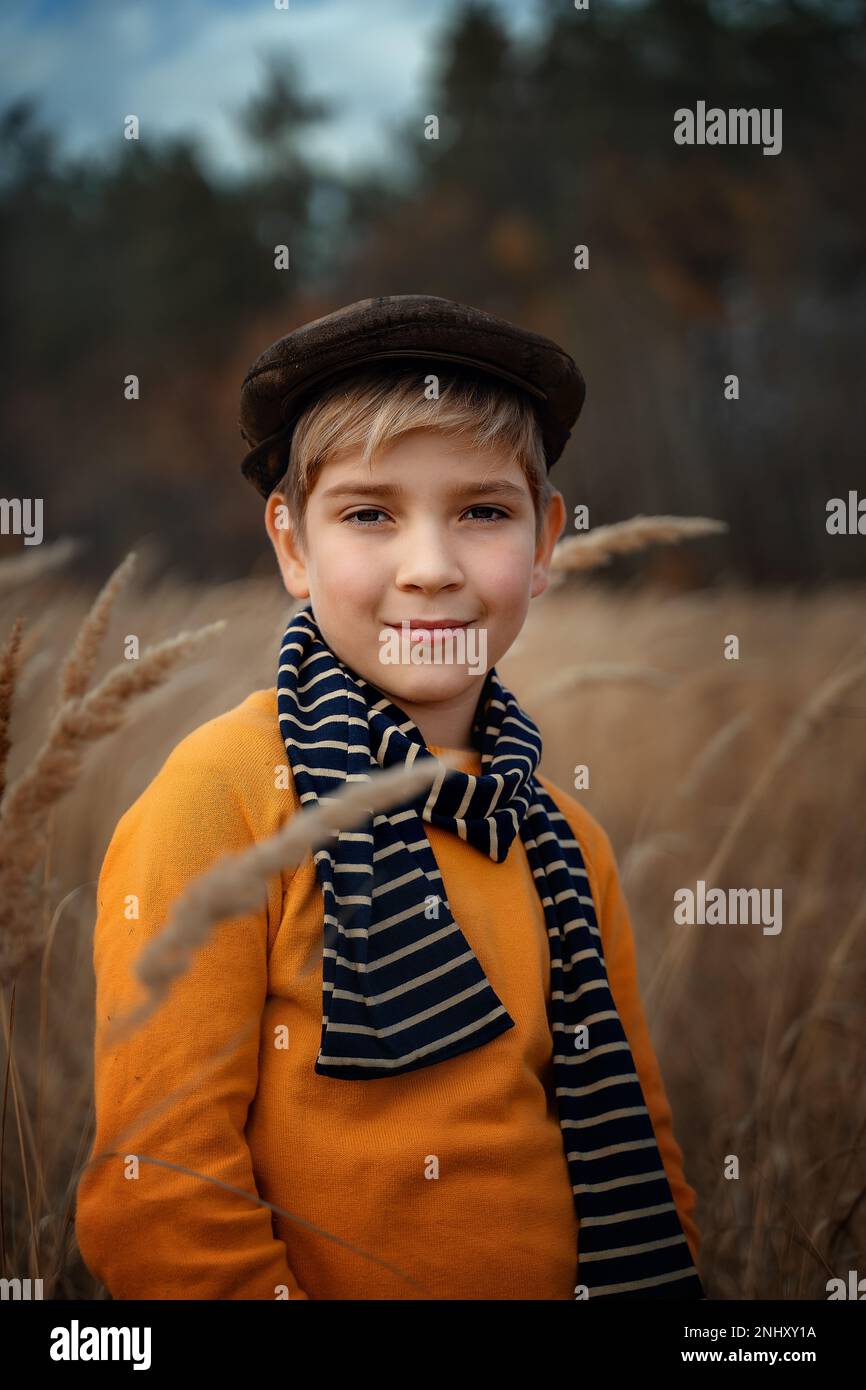 Ein lächelnder kleiner Junge in einer Mütze im Retro-Stil steht und lächelt. Kindermode, Retro-Style. Stockfoto