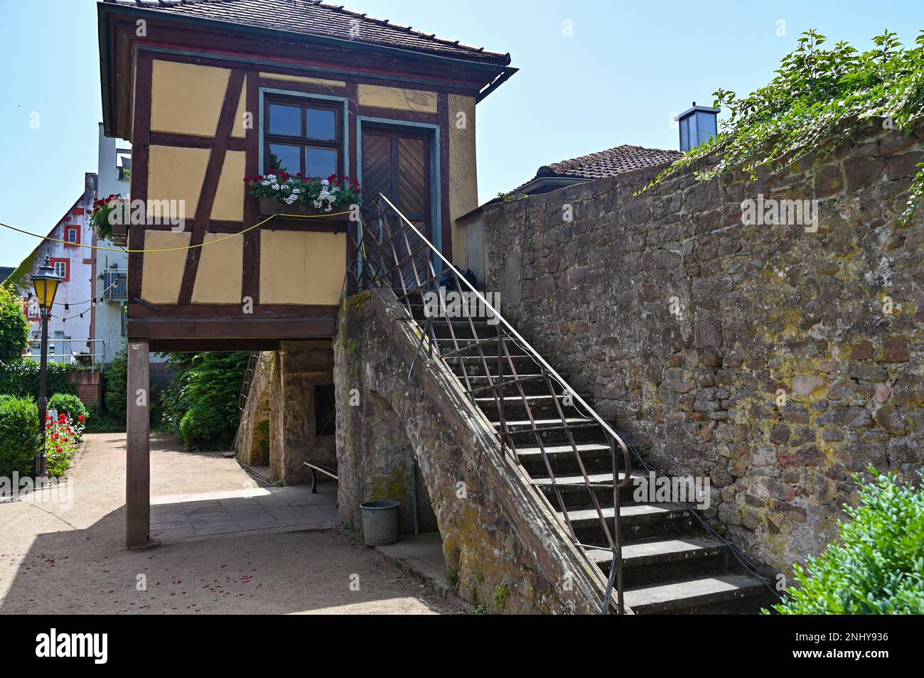 Treppe auf einer alten Steinmauer eines Schlosses im Sonnenlicht mit einem Fachwerkhaus Stockfoto