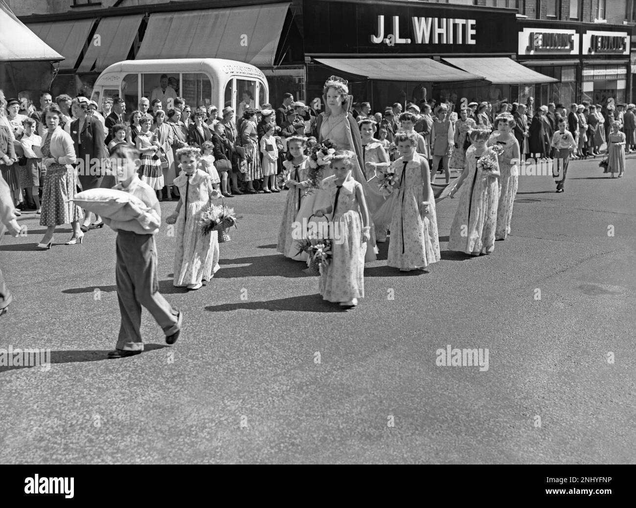 Eine Whit Walks-Prozession in Union Street, Oldham, Greater Manchester, Lancashire, England, UK c.1960. Eine „Rose Queen“ trägt ihre Krone und ist von Kindern umgeben, die Blumen tragen. Im Hintergrund befindet sich ein O'Donnell's Eiswagen. Die religiöse Veranstaltung in der Church of England fand traditionell am Whit Friday statt, an dem Kinder zusammen mit Messingbändern und Silberbändern beteiligt waren. Dieses Foto stammt aus einem alten Schwarz-Weiß-Negativ – einem klassischen 1950er/60s-Foto. Stockfoto