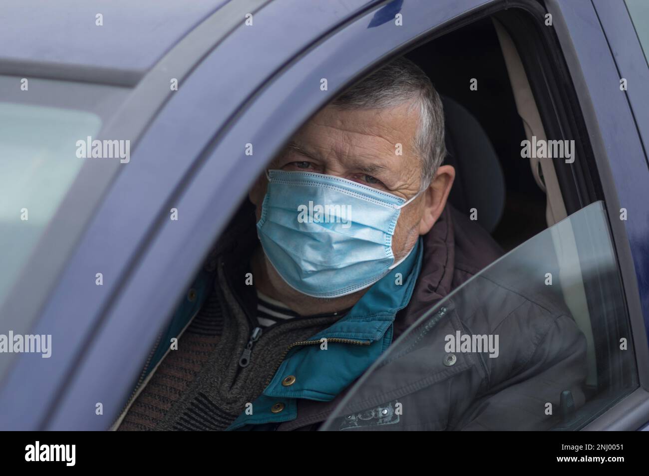 Porträt eines kaukasischen Senior-Fahrers, der eine Maske trägt, während er in seinem Auto sitzt Stockfoto