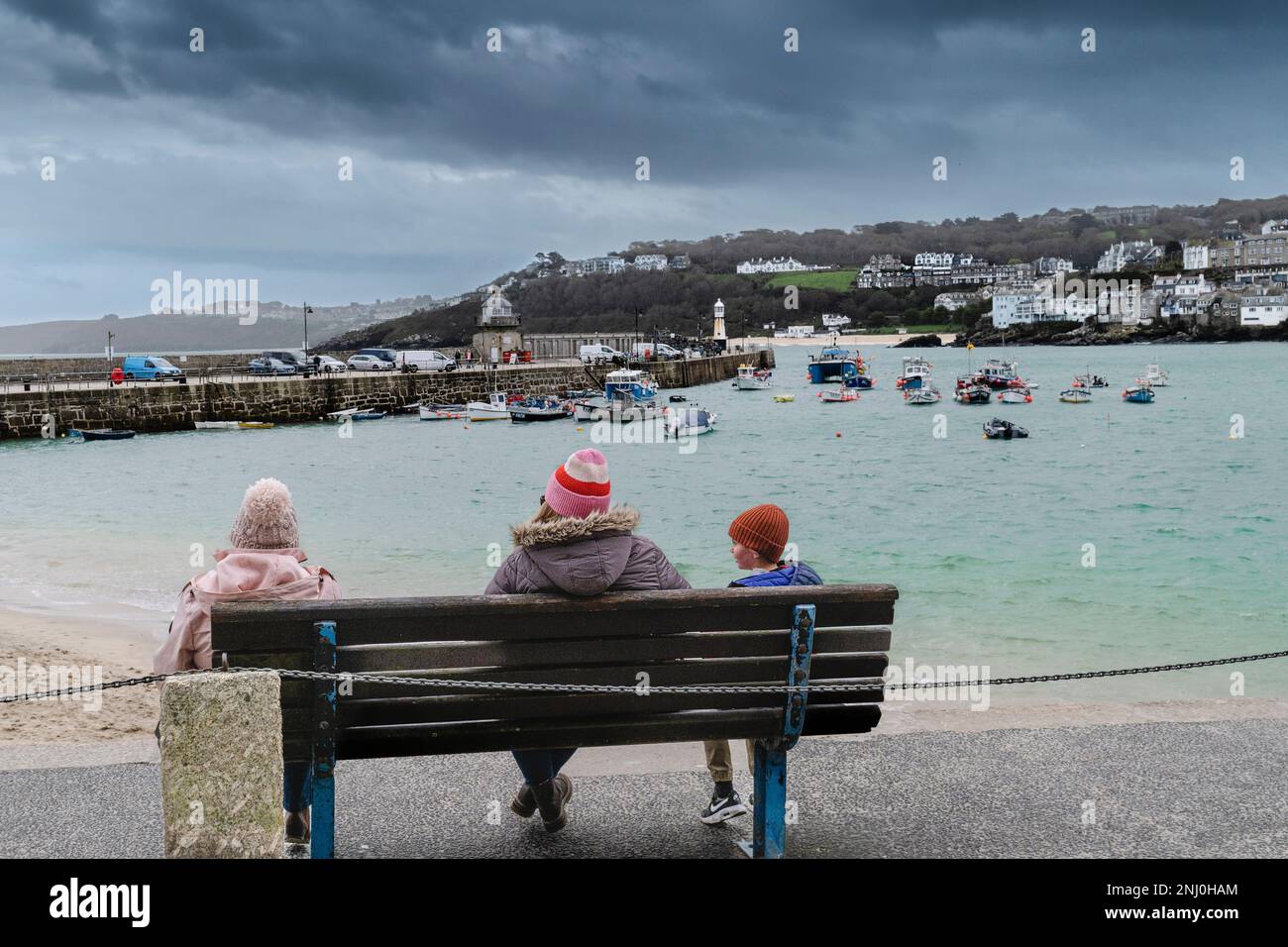 Wetter in Großbritannien. Besucher sitzen an einem regnerisch kalten, miserablen Tag auf einer Bank in der historischen Küstenstadt St. Ives in Cornwall, England, Großbritannien. Stockfoto