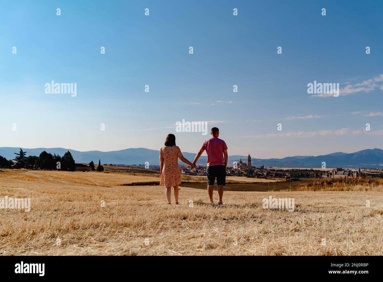 Ein hübsches Paar, das Händchen hielt und durch eine gelbe, trockene Wiese in Spanien ging Stockfoto