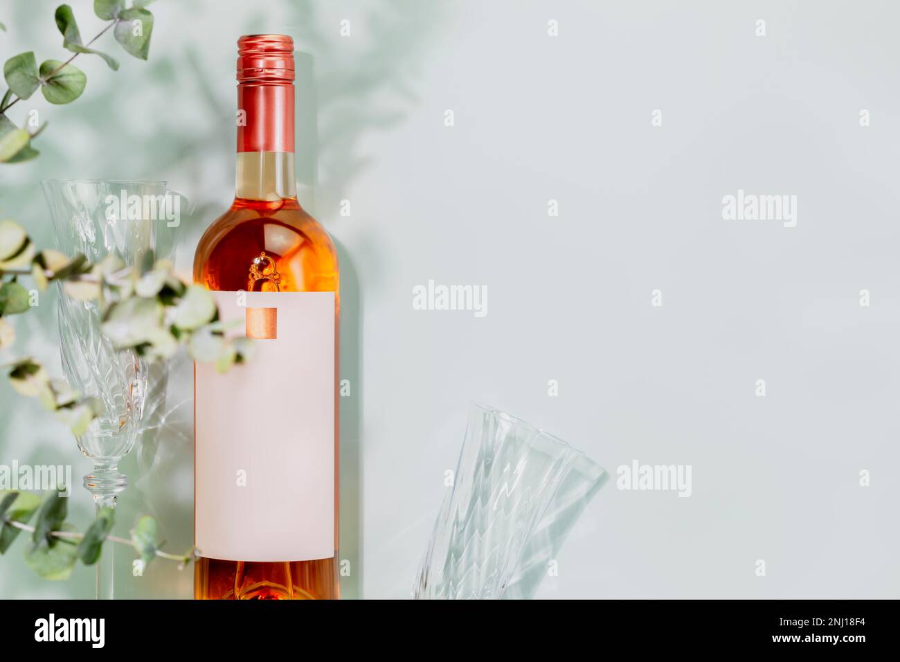 Biologischer Rosenwein. Flasche natürlicher Rosa Wein mit Weingläsern auf blauem Hintergrund mit Eukalyptusblättern. Sommer romantisches Stillleben mit einer Flasche Stockfoto