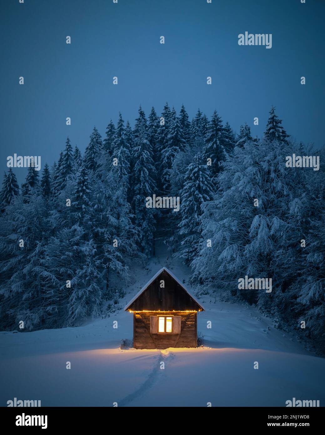 Fantastische Winterlandschaft mit glühender Holzhütte im verschneiten Wald. Gemütliches Haus in den Karpaten. Weihnachtsfeiertagskonzept Stockfoto
