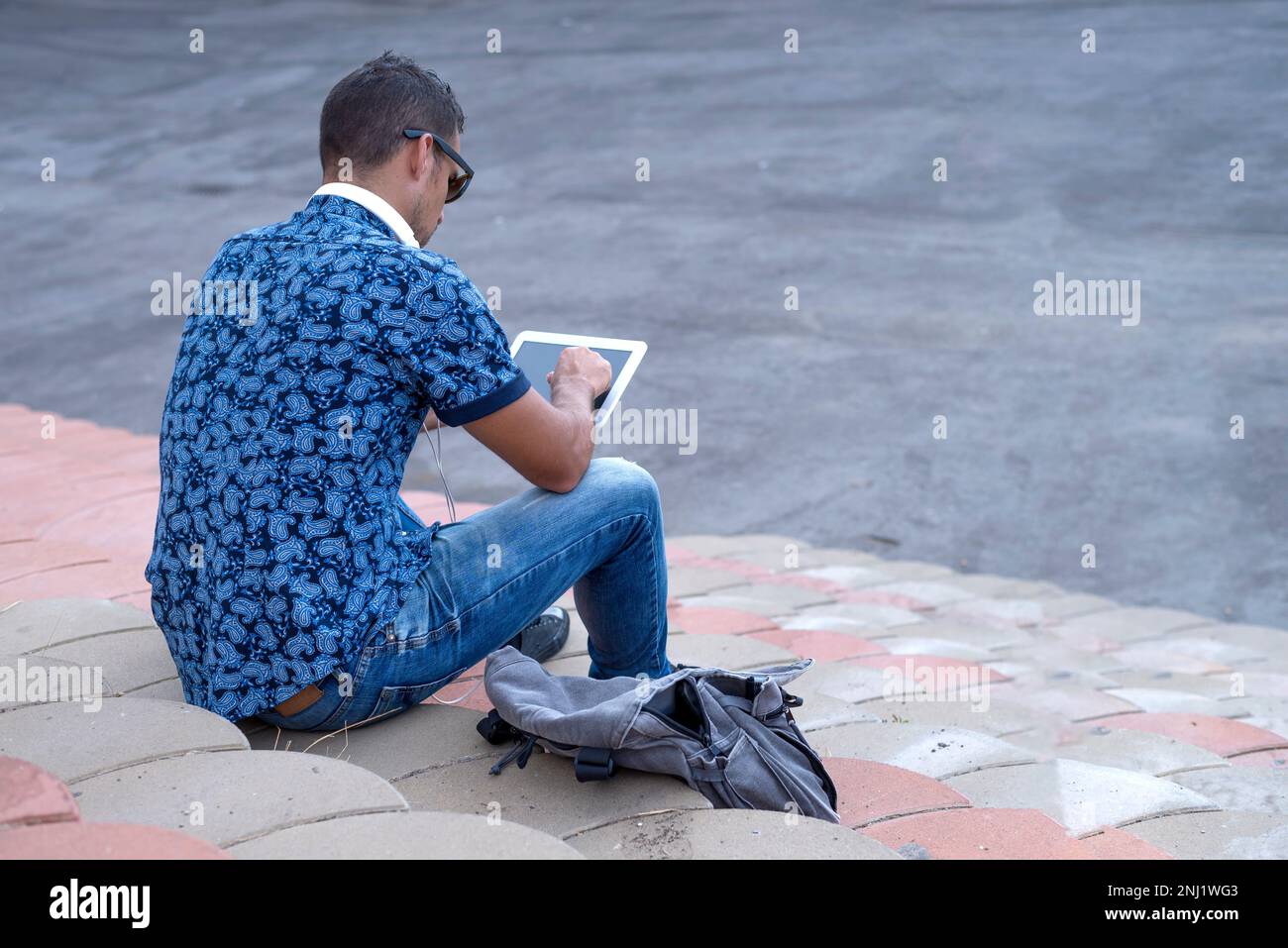 Ein rückwärtiges Bild eines jungen Mannes, der mit einem Tablet auf einer Tribüne sitzt Stockfoto