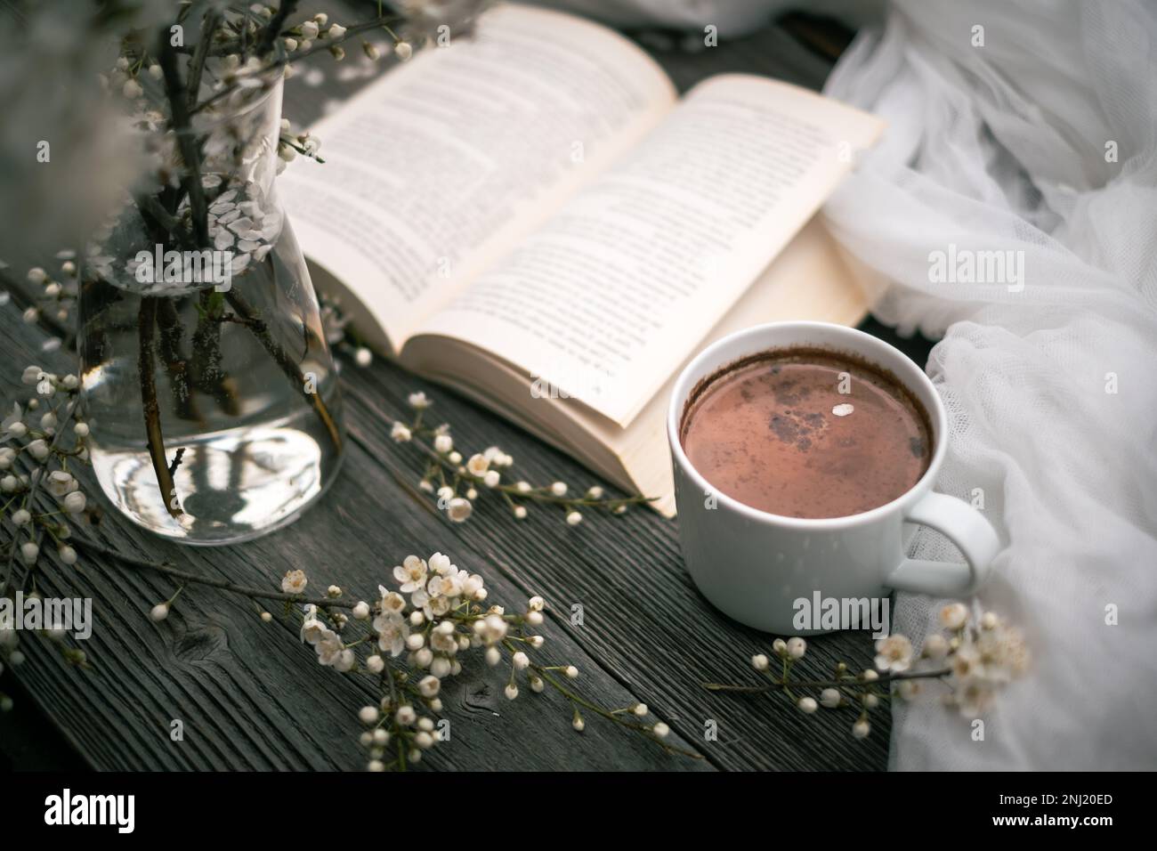 Tasse Kakao, altes Buch und Kirschblüten auf Holzhintergrund. Lesekonzept Stockfoto